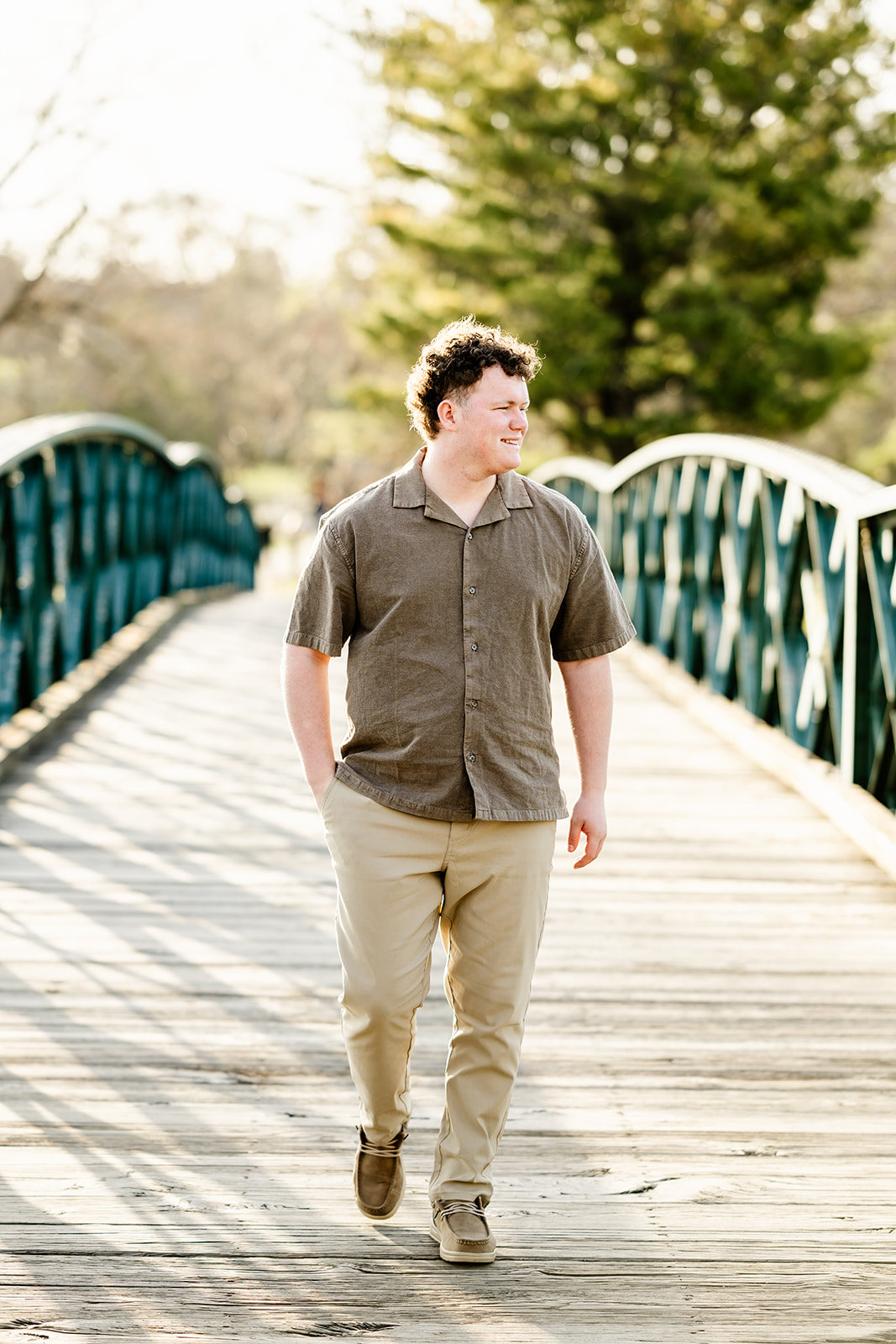 A high school senior in khakis and brown shirt walks a wooden bridge smiling with a hand in pocket after enjoying ACT Prep in Chicago