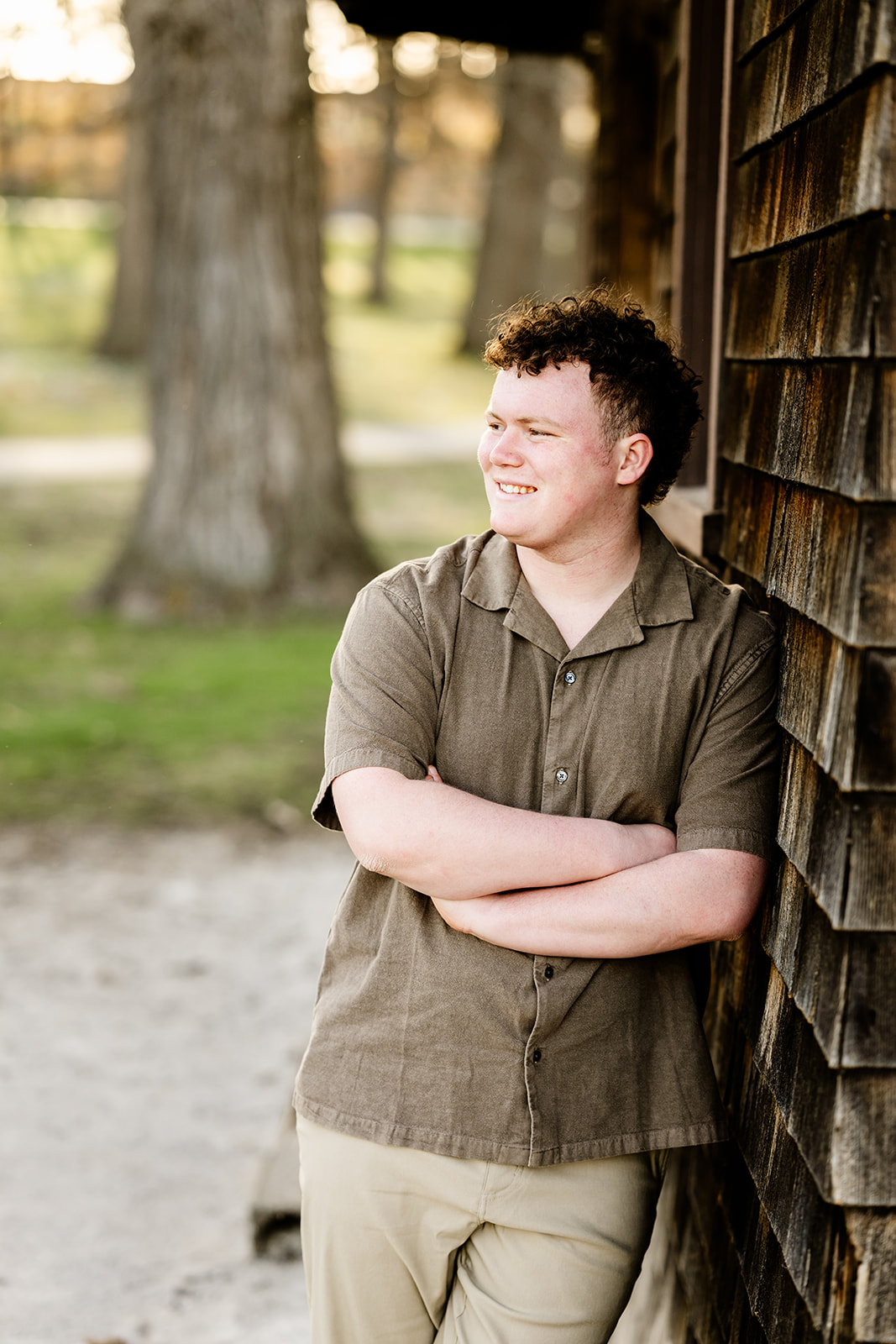A high school senior leans on a rustic wooden wall in a brown shirt and arms crossed after finding ACT Prep in Chicago