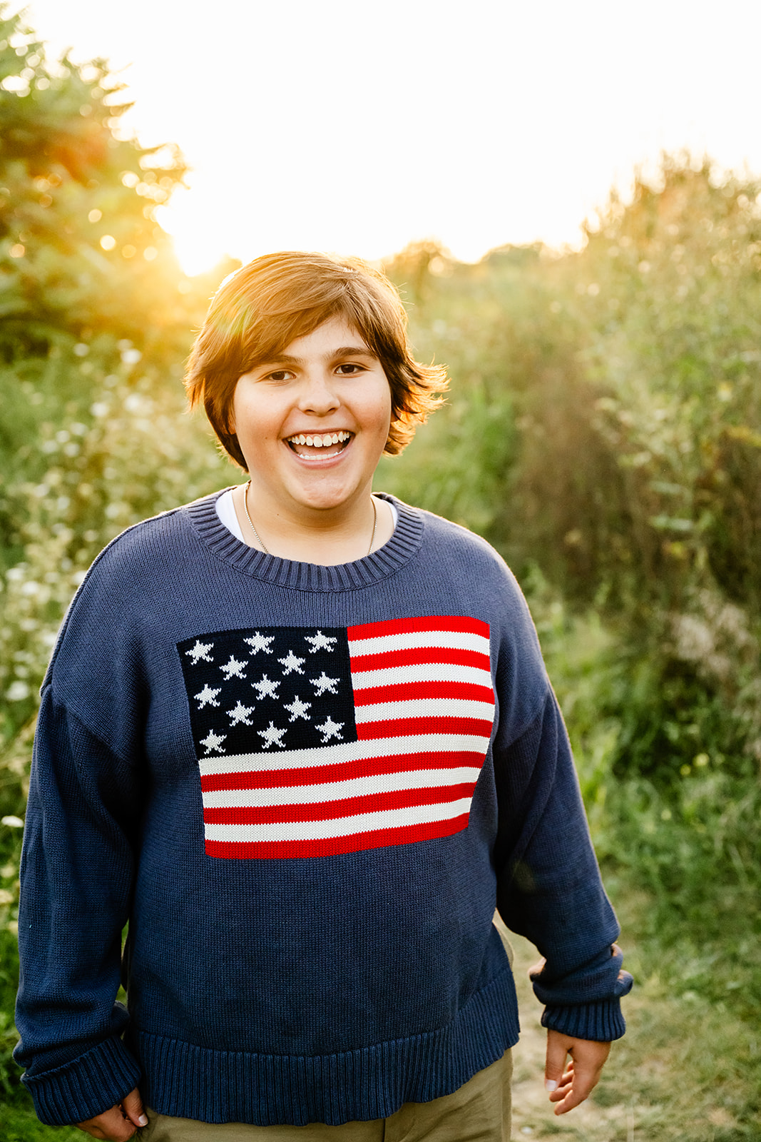A high school senior laughs while walking in a park trail at sunset in an american flag sweater after using ACT prep in Naperville