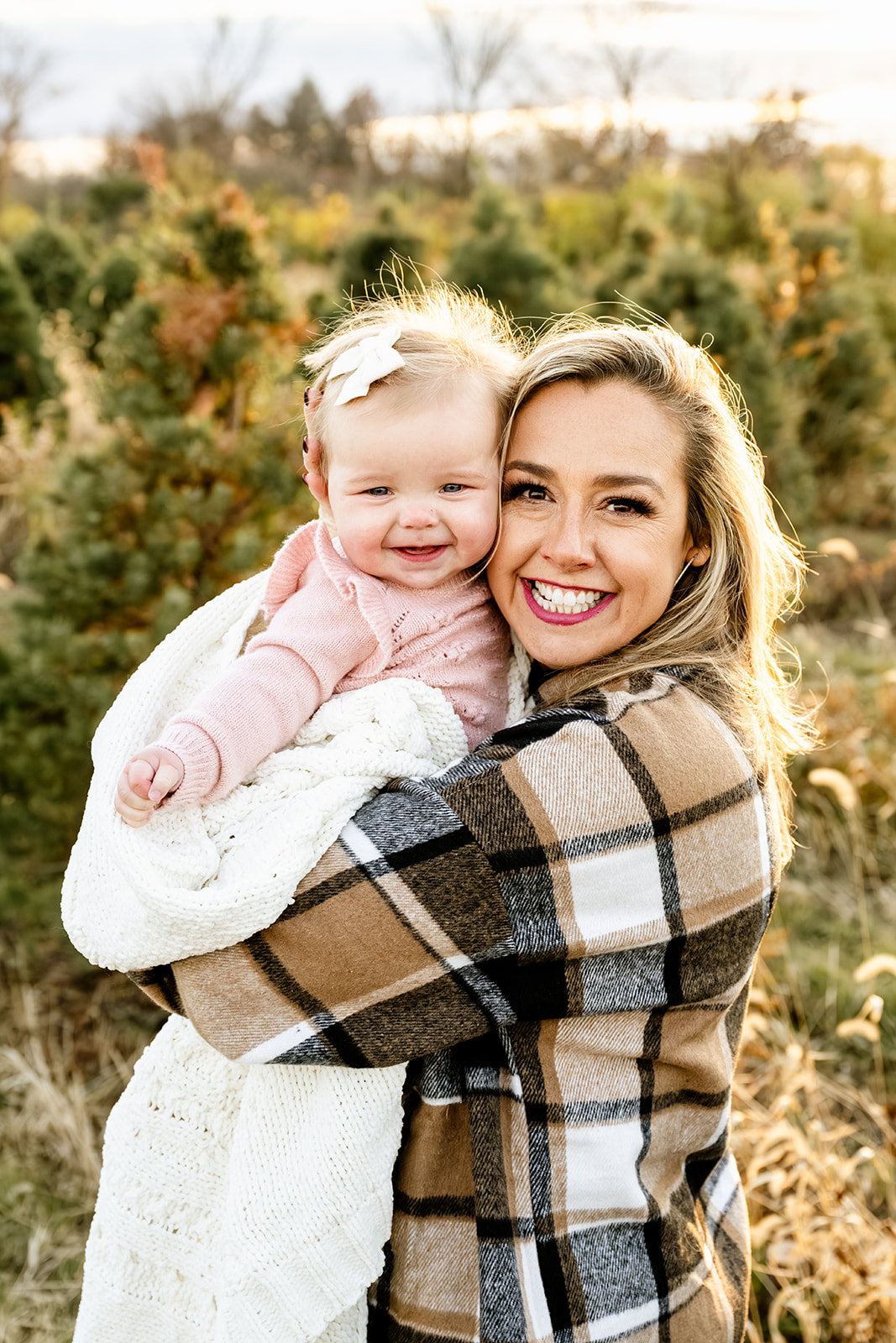 A happy mom in a plaid shirt smiles while hugging her toddler daughter wrapped in a blanket after finding great daycares in Naperville