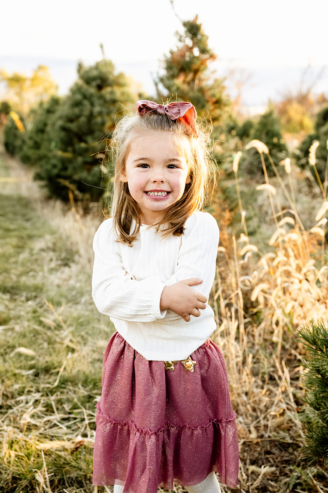 A happy toddler girl in a white shirt and pink dress in a christmas tree farm after visiting daycares in Naperville