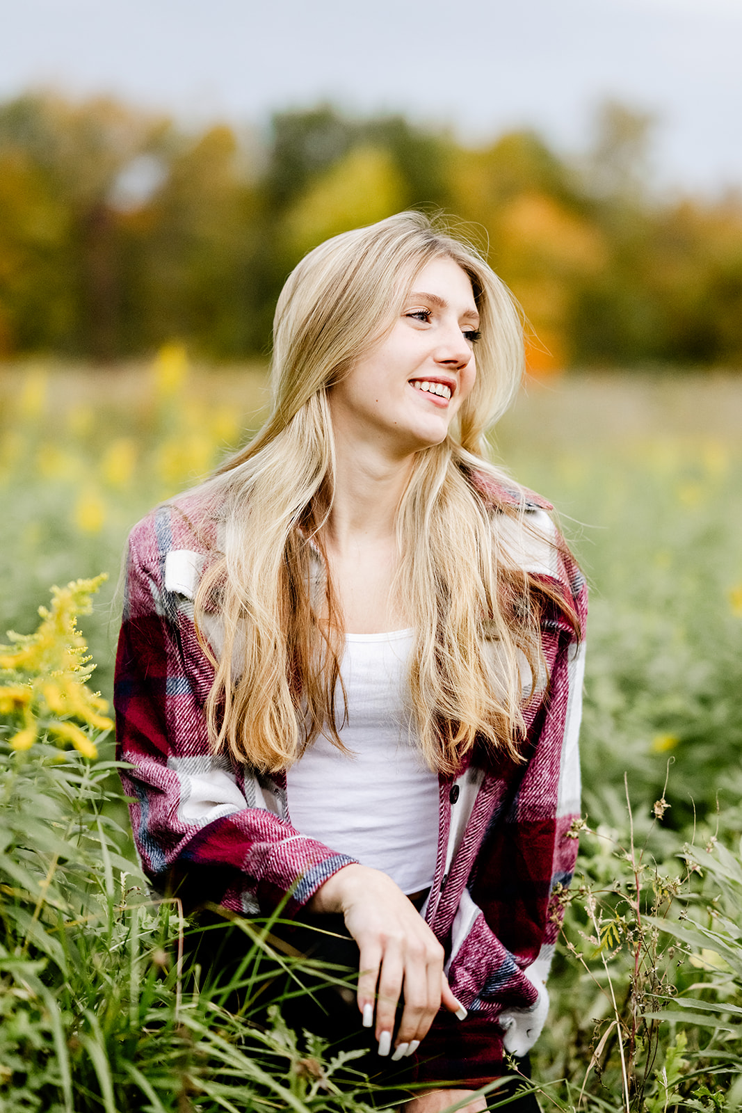 A blonde woman looks over her shoulder while smiling an sitting in tall grasses in a meadow