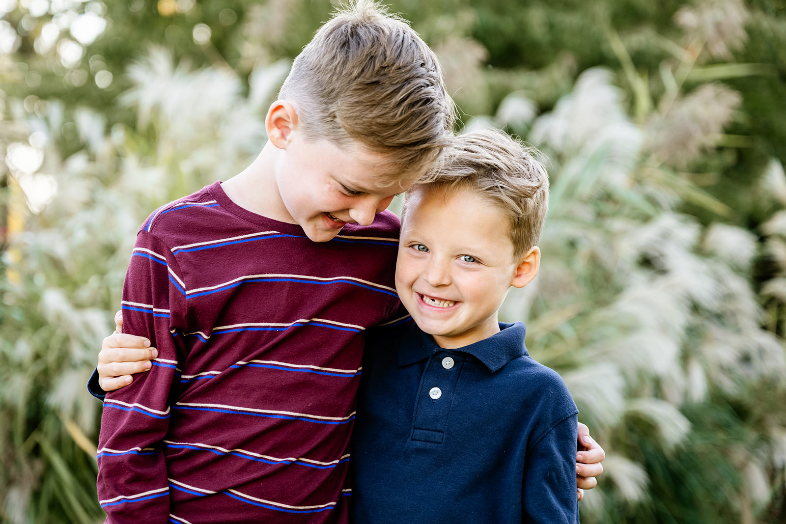 A young boy in a stripe shirt hugs his smiling younger brother in a blue polo in a park after attending private elementary schools in Chicago