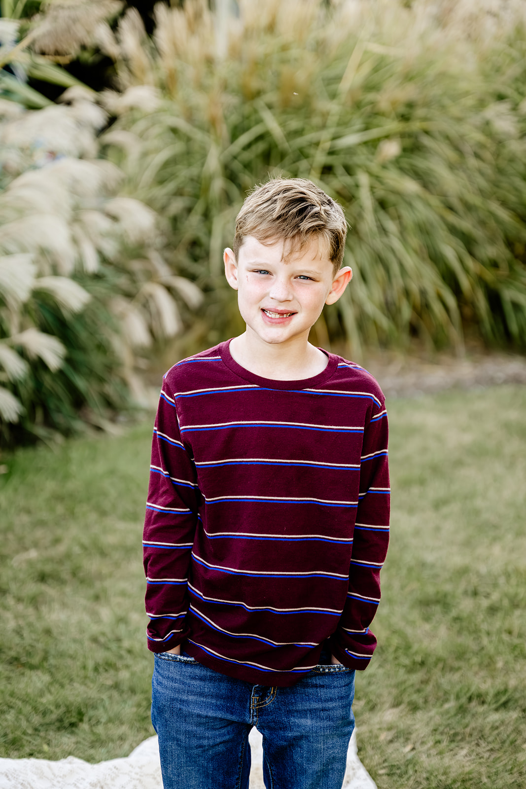 A young boy in a stripe maroon shirt stands in a lawn with hands in pockets and smiling after exploring private elementary schools in Chicago