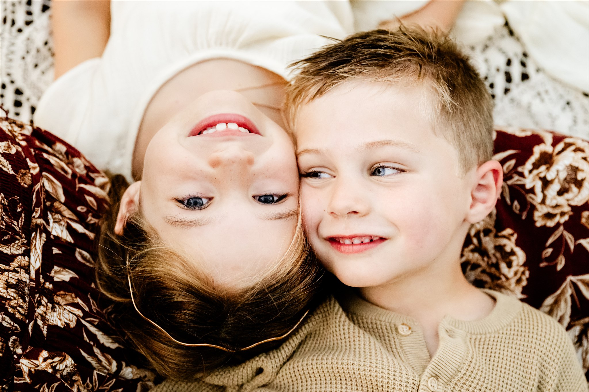 Toddler brother and sister smile while laying head to head touching cheeks on mom's lap after visiting private schools in Naperville