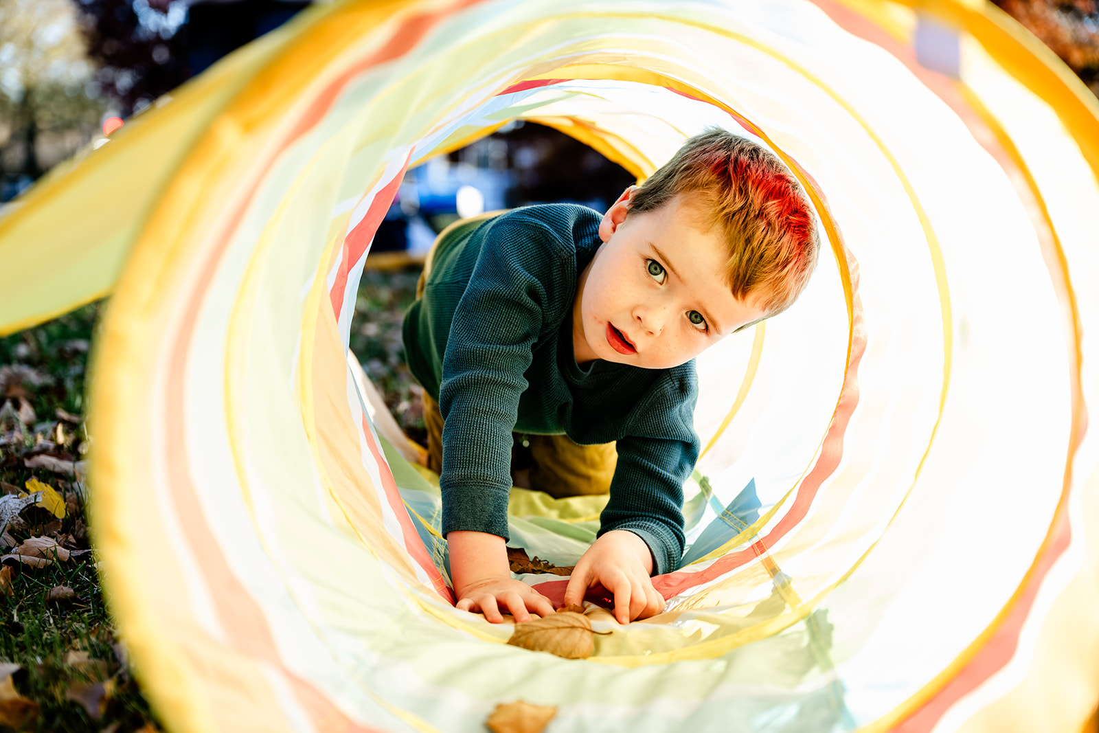 A toddler boy in a green shirt crawls through a colorful tube in a park before visiting Children's Museums in Naperville