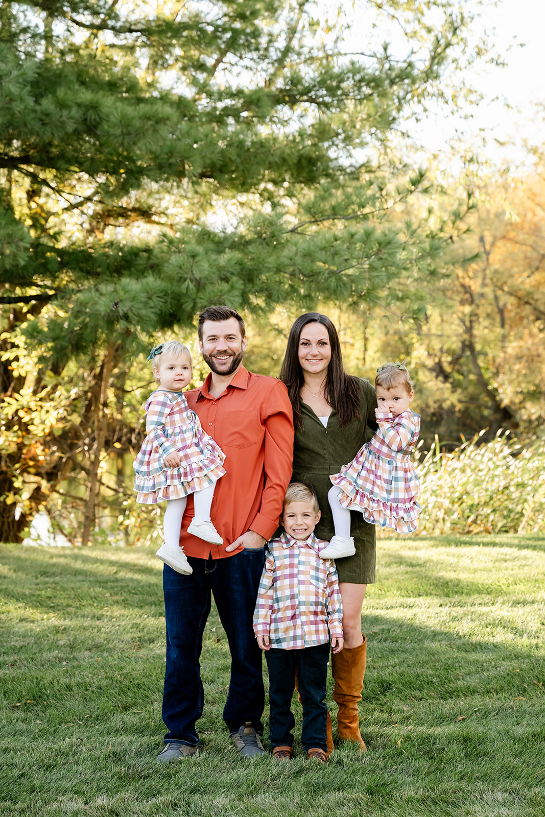 Mom and dad in green and red stand in a park lawn at sunset with three toddlers in matching shirt and dresses thanks to pediatric chiropractors in Naperville