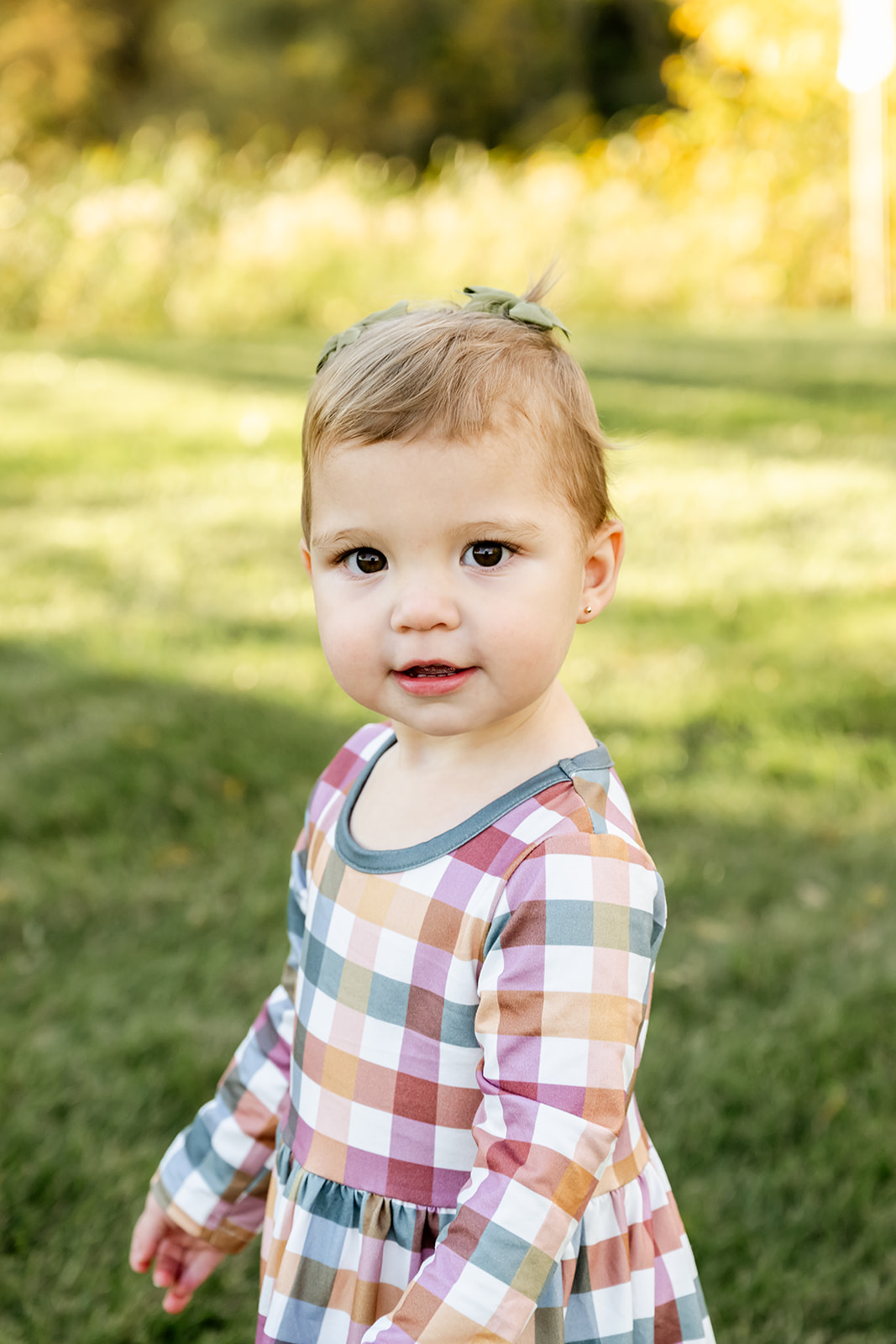 A toddler girl in a colorful dress walks in a park with a smile thanks to pediatric chiropractors in Naperville