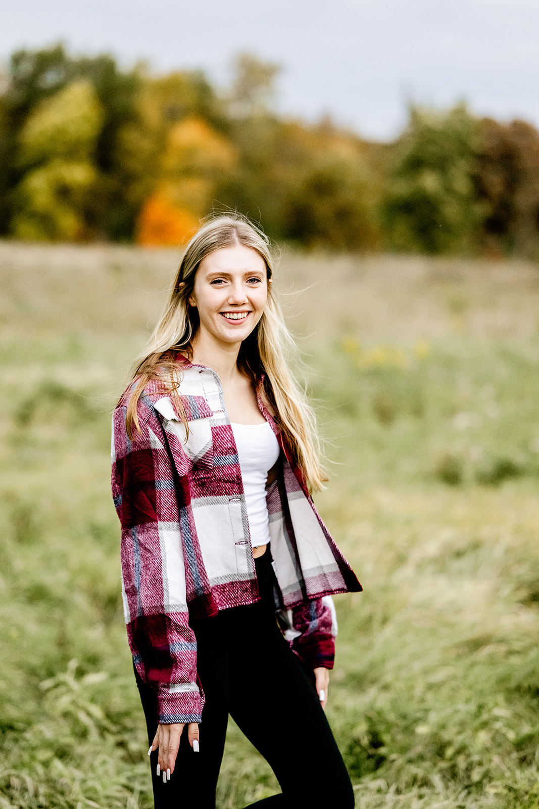 A high school senior in a plaid shirt walks in a meadow at sunset while smiling after visiting graduation party venues in Naperville