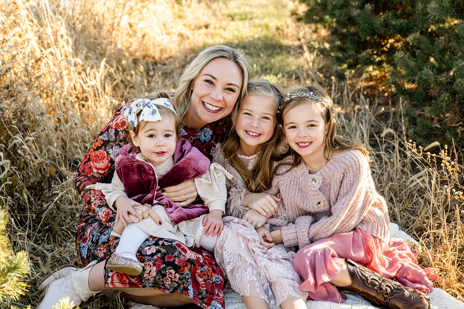 A happy mom in a flower print dress sits on a picnic blanket smiling with her three smiling toddler daughters in pink while staying at kid-friendly hotels in Chicago