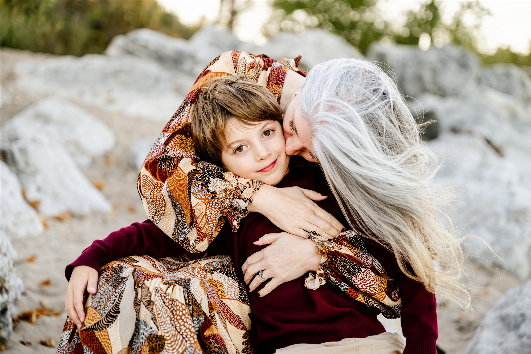 A mother in a dress hugs and kisses the cheek of her smiling toddler on a windy beach after some mommy and me classes in Naperville