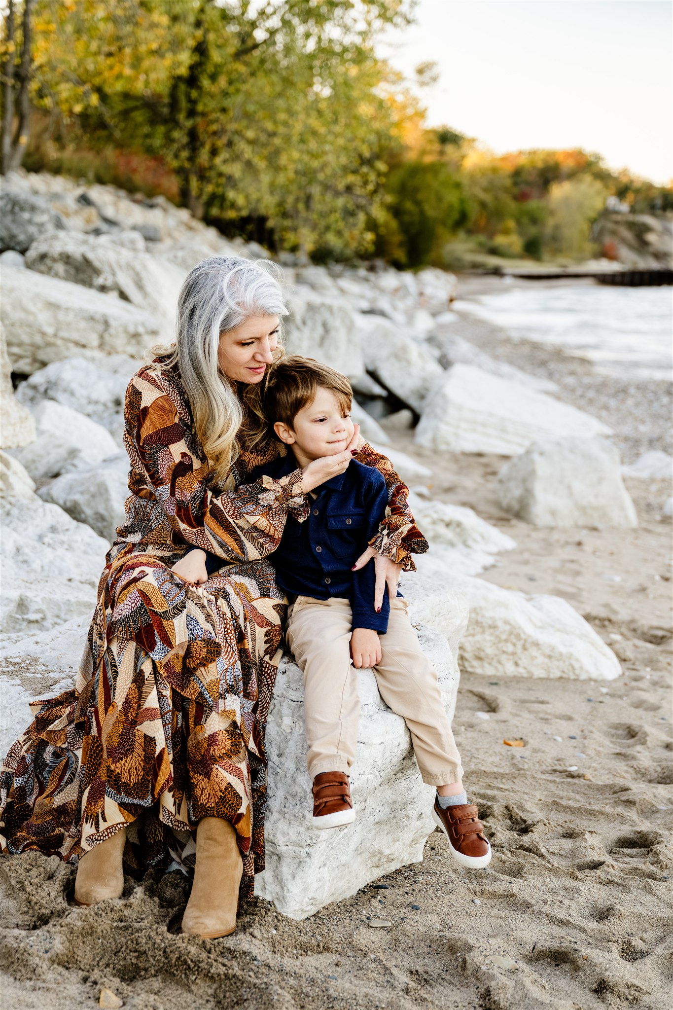 A mother cuddles her happy toddler son on a rock on the beach after some mommy and me classes in Naperville