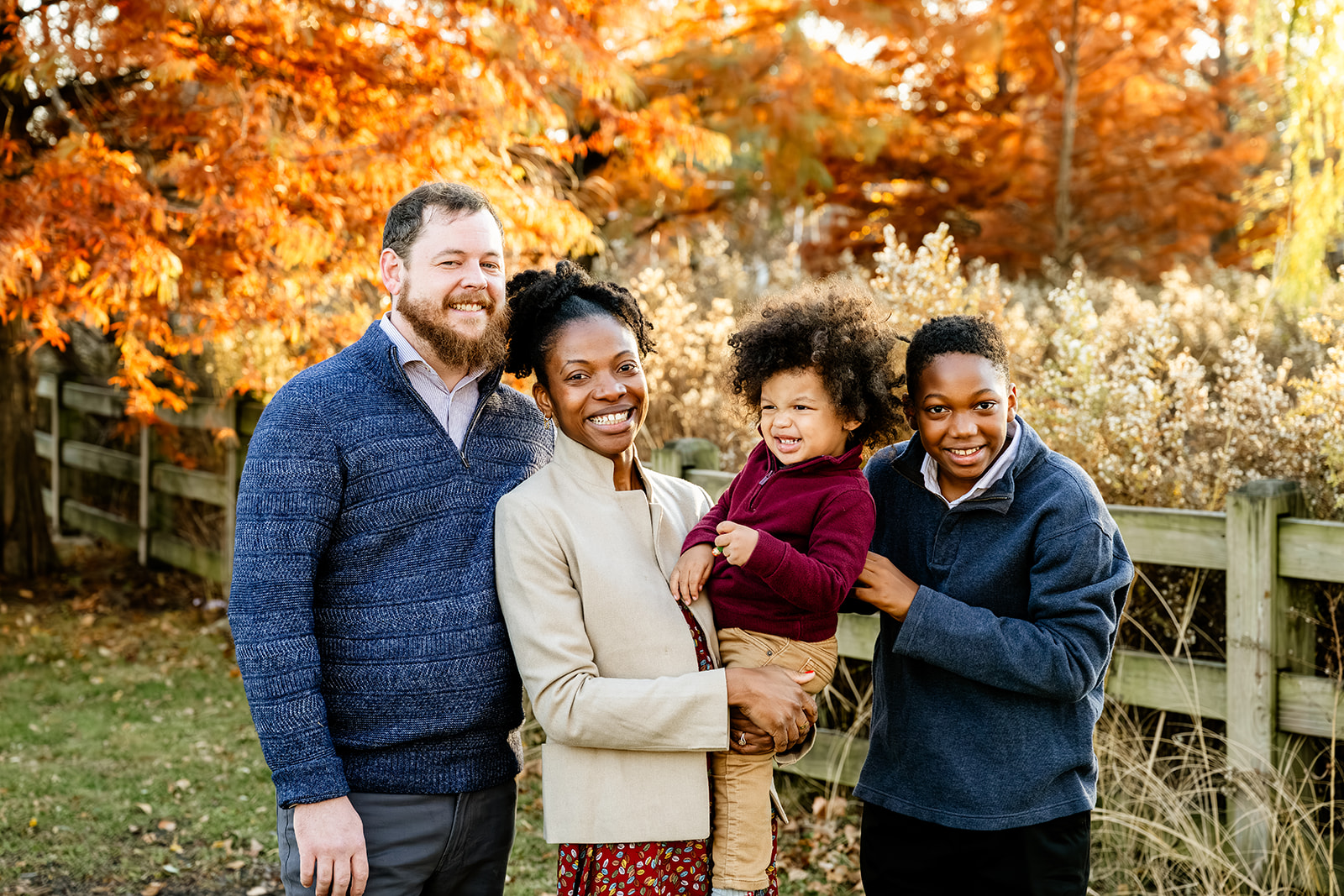 Happy mom and dad stand in a park in fall wearing sweaters after finding North Shore Nannies