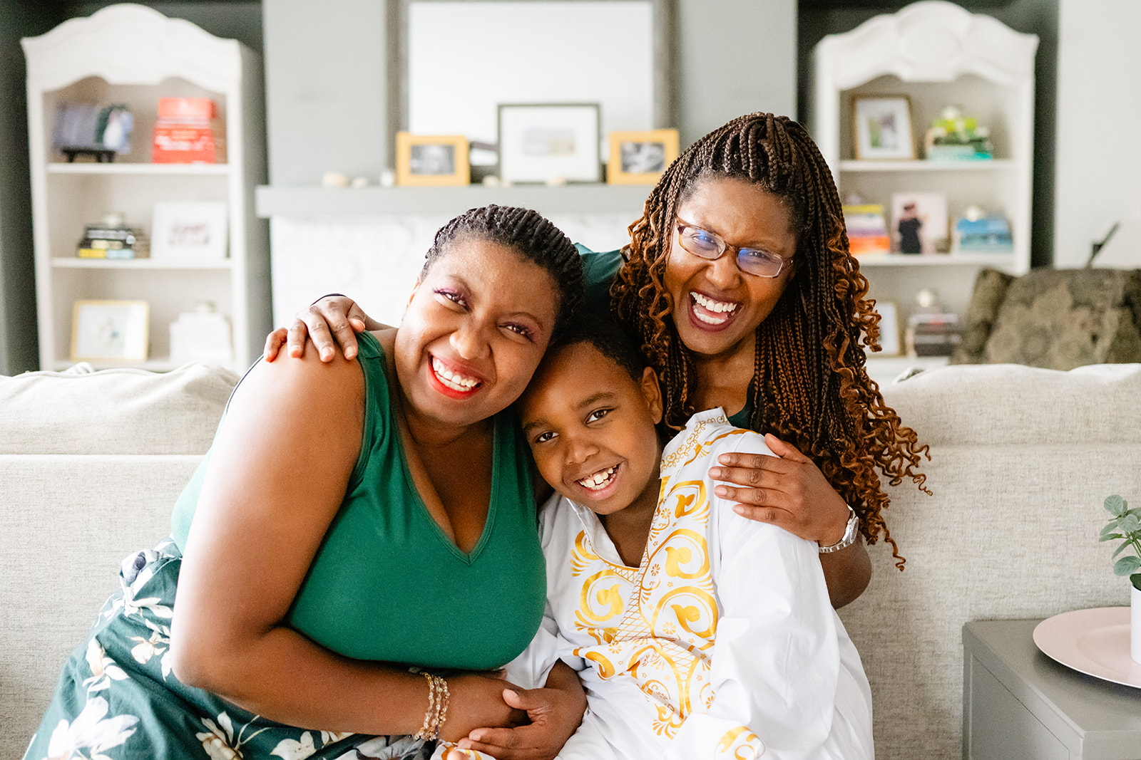Happy moms hug their son in a white and gold traditional blouse in a living room with big smiles