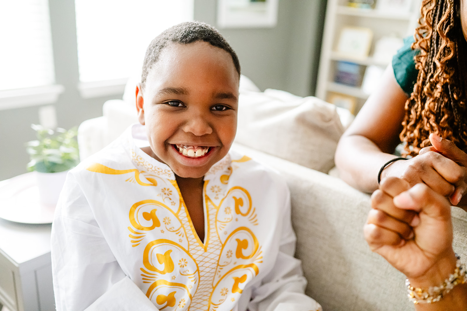 A happy young child in a white shirt sits on a couch smiling after visiting a pediatric dentistry in North Shore