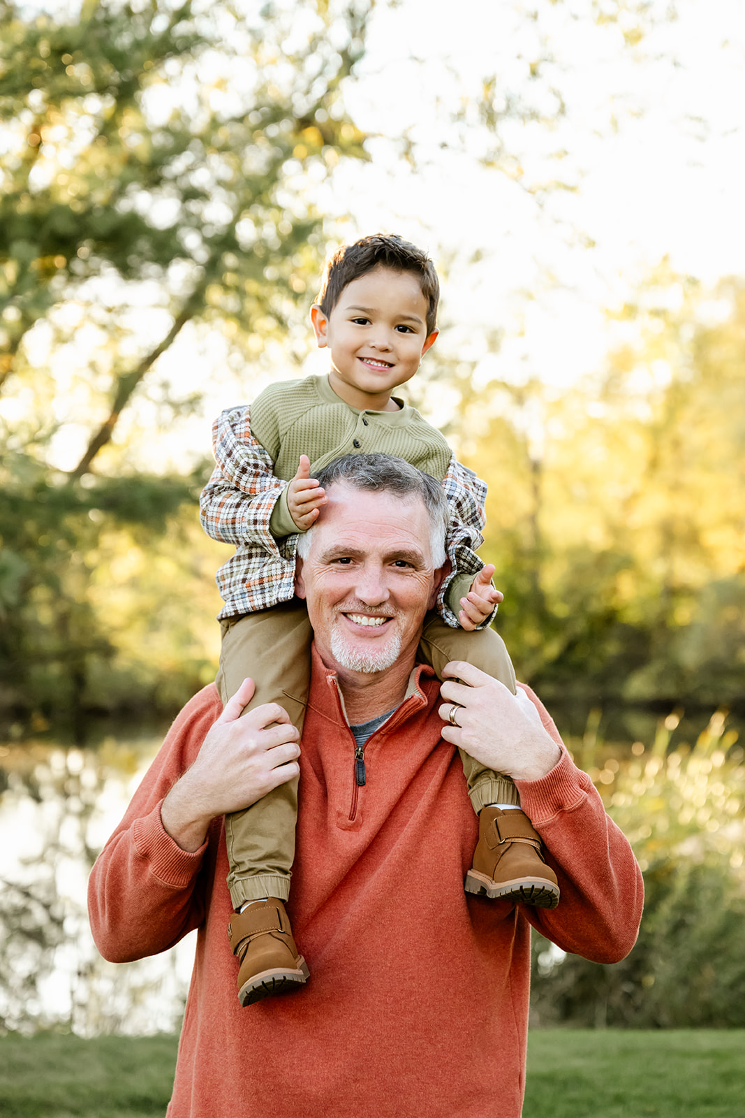 A happy dad stands in a park with his toddler son on his shoulders