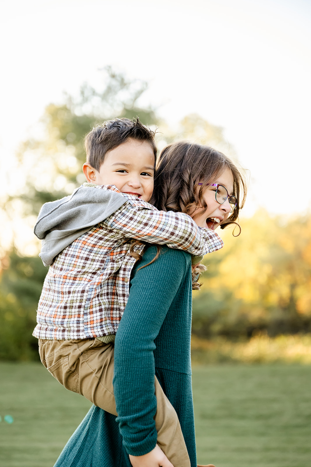 A happy toddler boy gets a piggy back ride from big sister in a park at sunset after some play therapy in Chicago