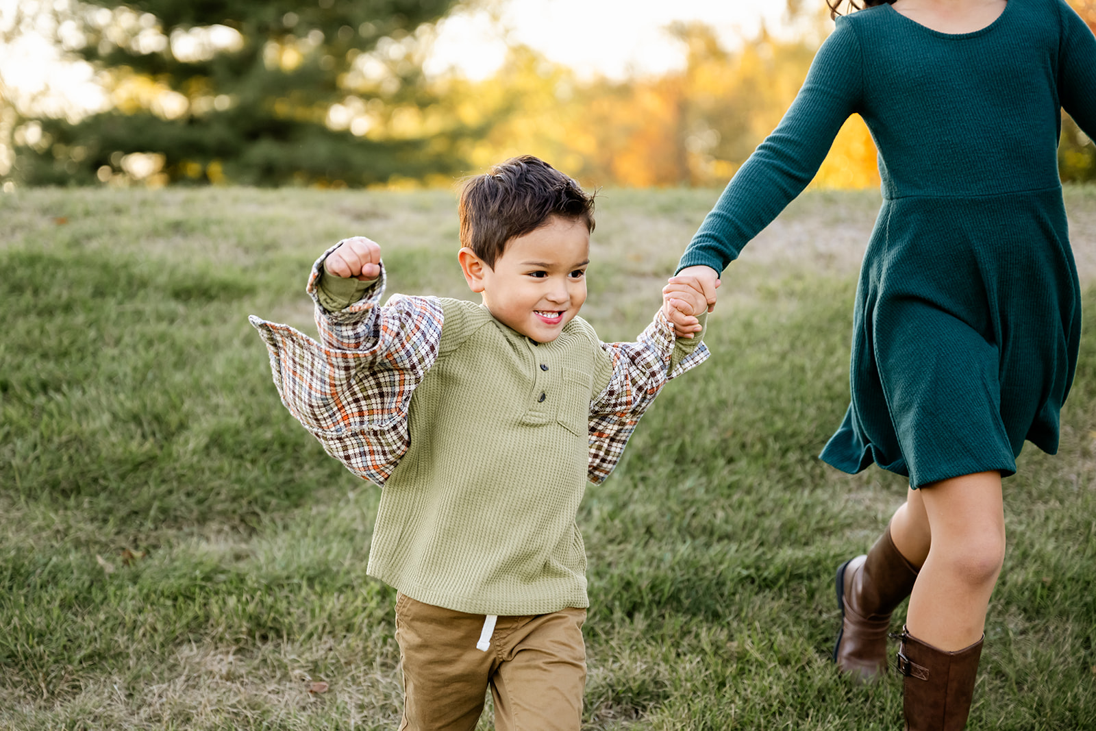 A toddler boy in a green shirt runs while holding hands with big sister in a park at sunset after some play therapy in Chicago