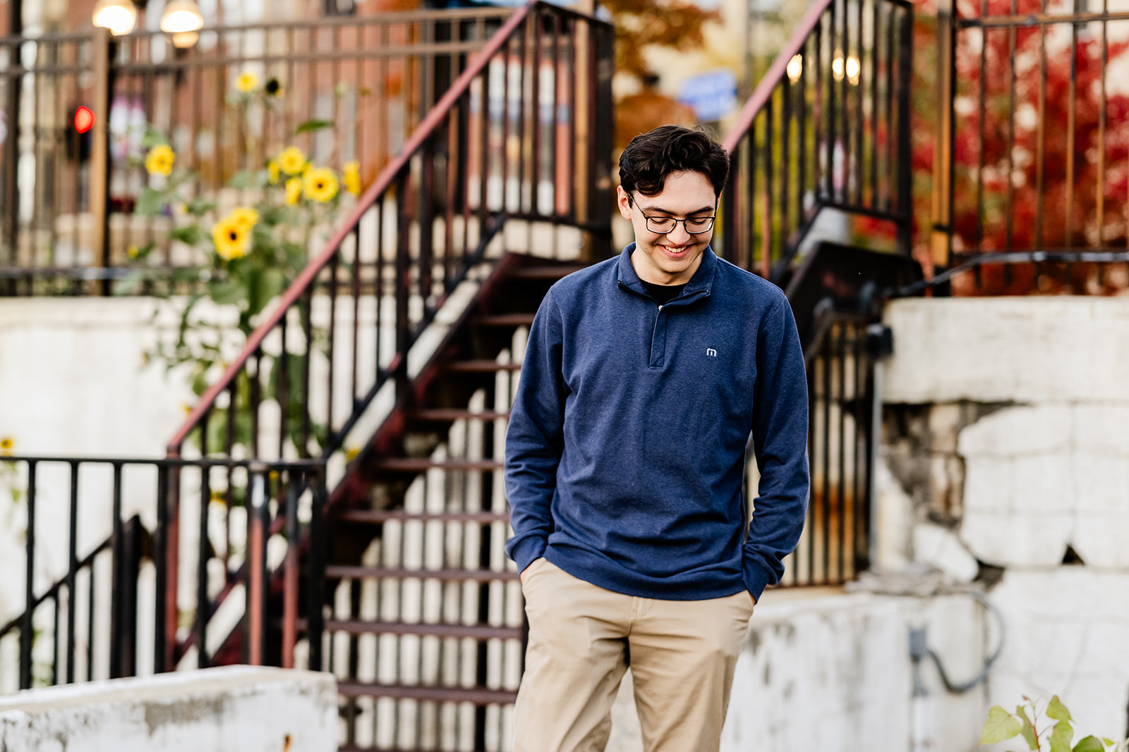 A teenager smiles down while walking a metro area with sunflowers in a blue sweater with hands in pockets after using tutors in North Shore