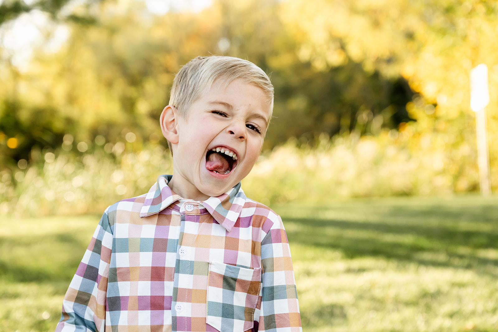 A toddler boy in a plaid shirt makes a silly face in a park at sunset after finding great daycares in North Shore