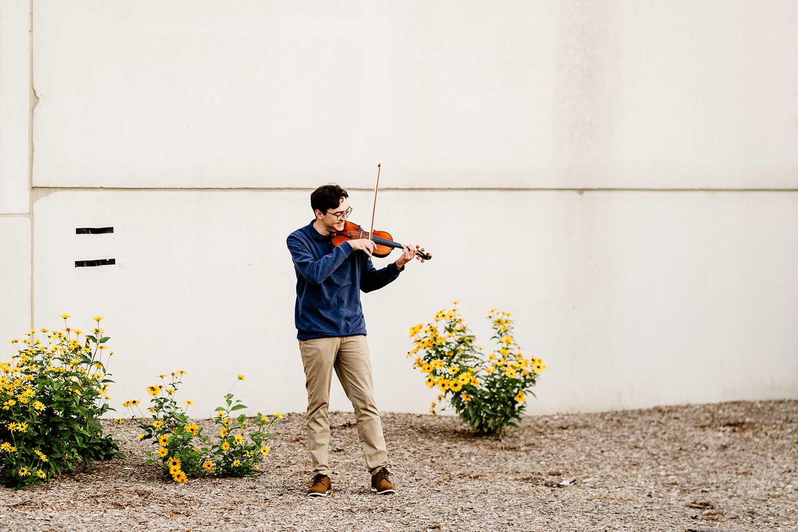 A high school senior in a blue sweater plays violin in a garden at one of the graduation party venues in Chicago
