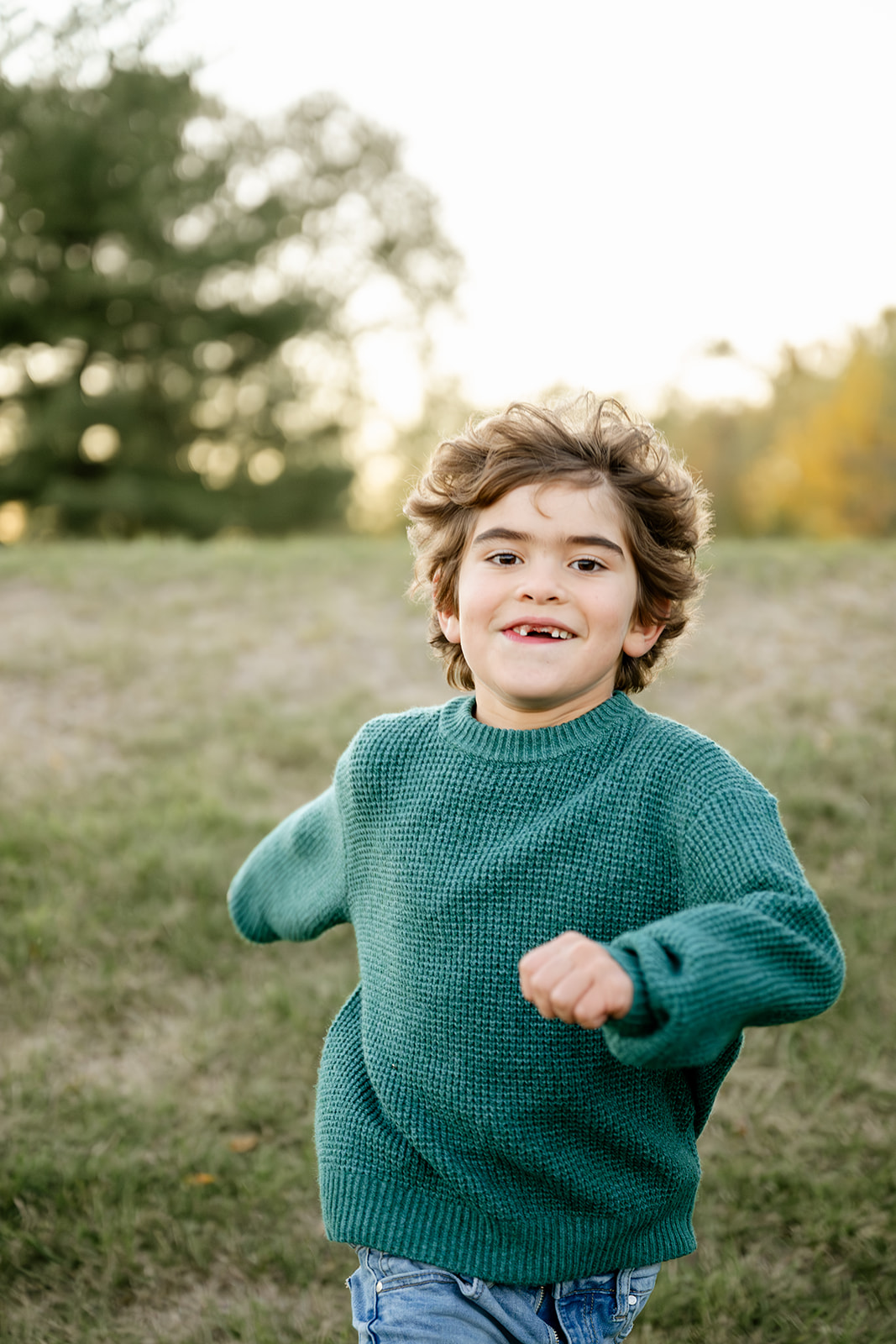 A young boy missing his front teeth runs in a park in a green sweater at sunset before visiting indoor playgrounds in North Shore