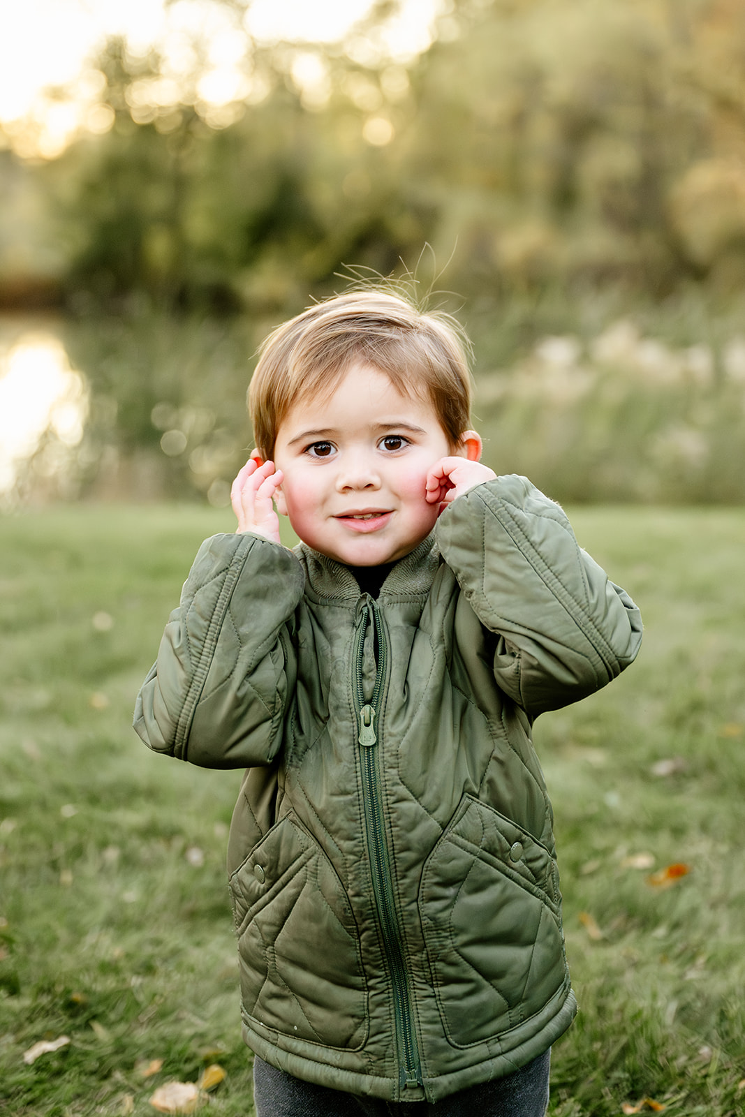 A toddler in a green jacket playing in a lawn at sunset after visiting indoor playgrounds in North Shore