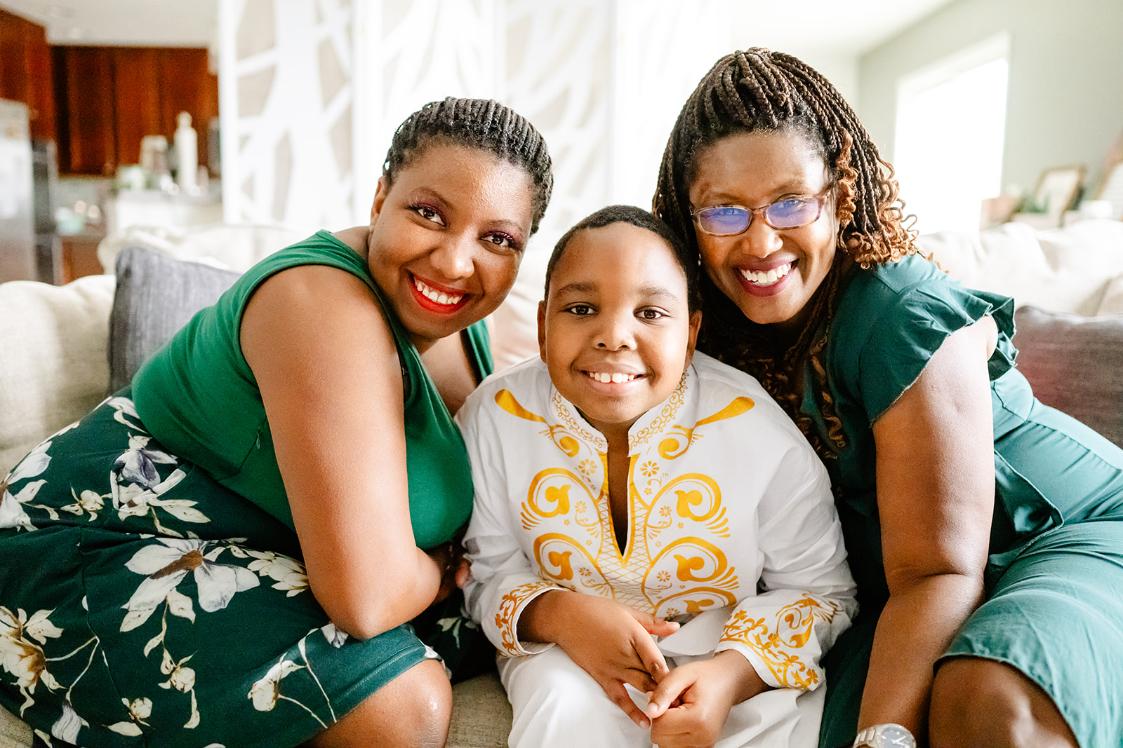 A happy young boy in a white and gold outfit sits with his moms on a couch smiling thanks to occupational therapy in Naperville