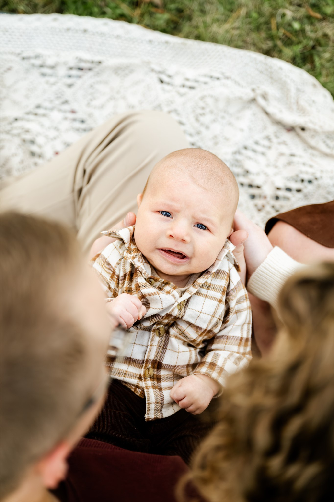 A toddler lays in mom and dad's laps in a plaid shirt in a park on a picnic blanket thanks to pediatric occupational therapy in Chicago