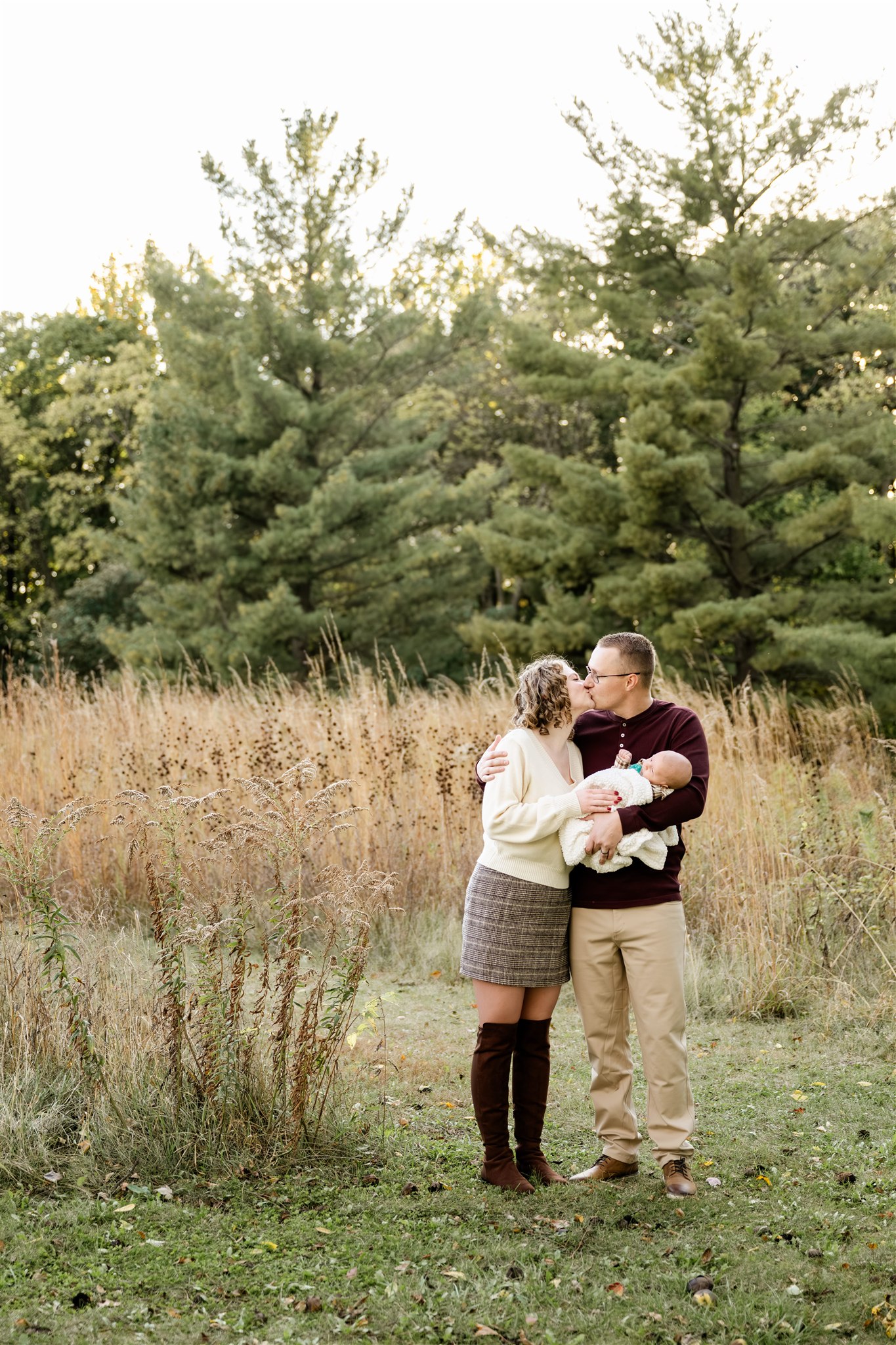 Happy new parents hold their infant while standing in a park kissing at sunset after some pediatric occupational therapy in Chicago