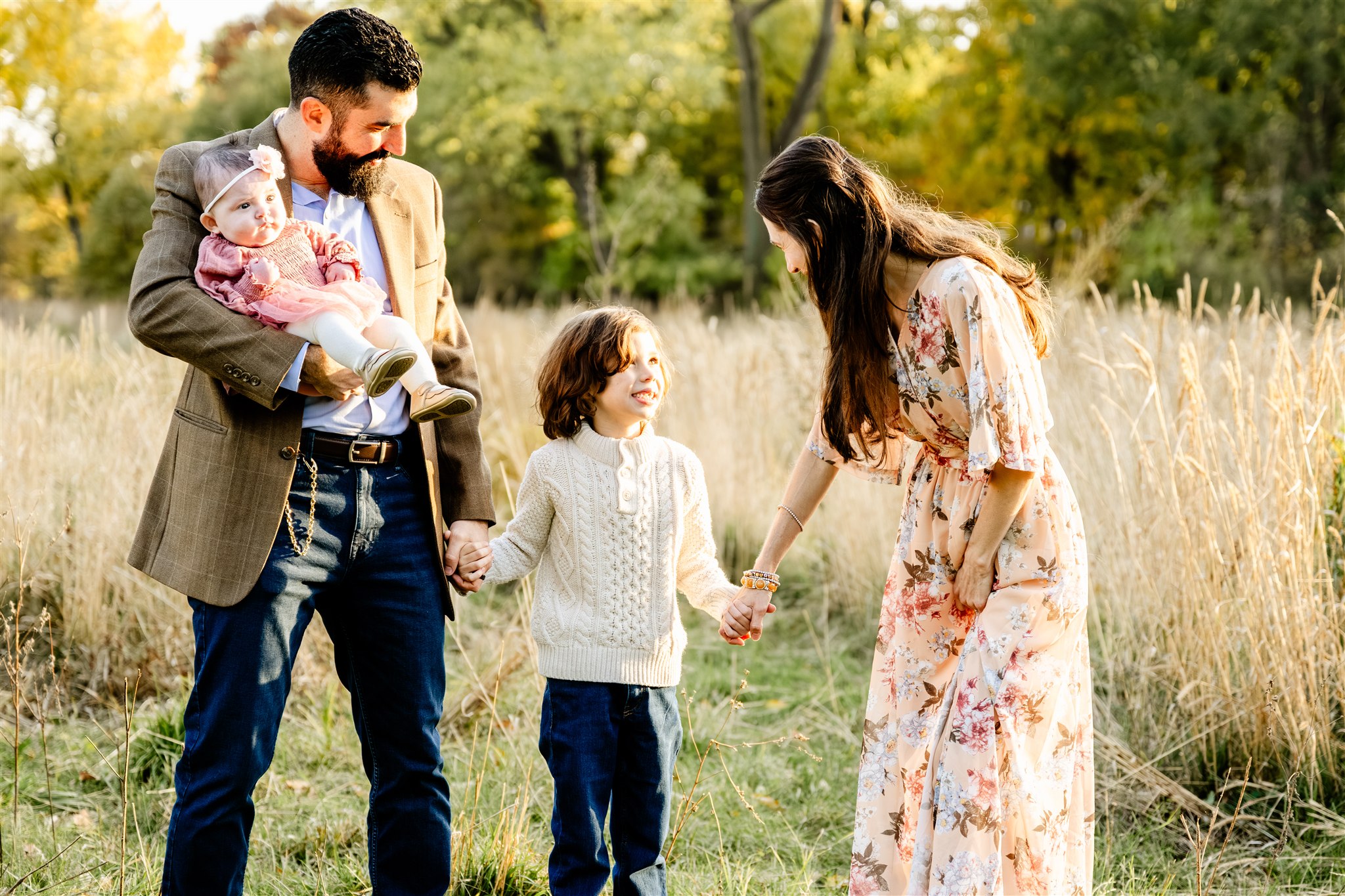 A toddler in a white sweater walks with mom and dad in a park through tall grasses after visiting pediatricians in North Shore