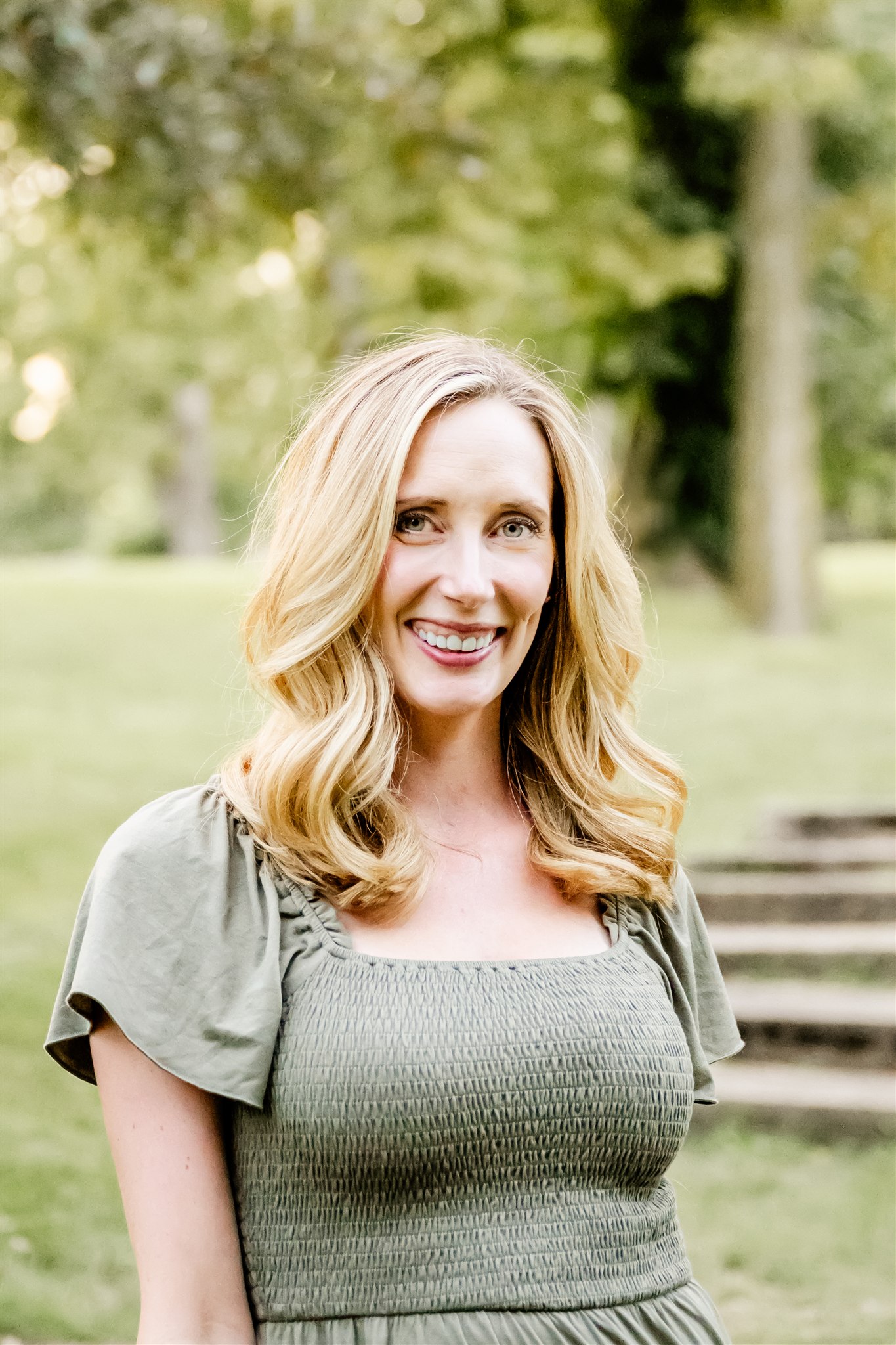 A happy mother in a green dress stands in a park lawn smiling after some pilates classes in North Shore