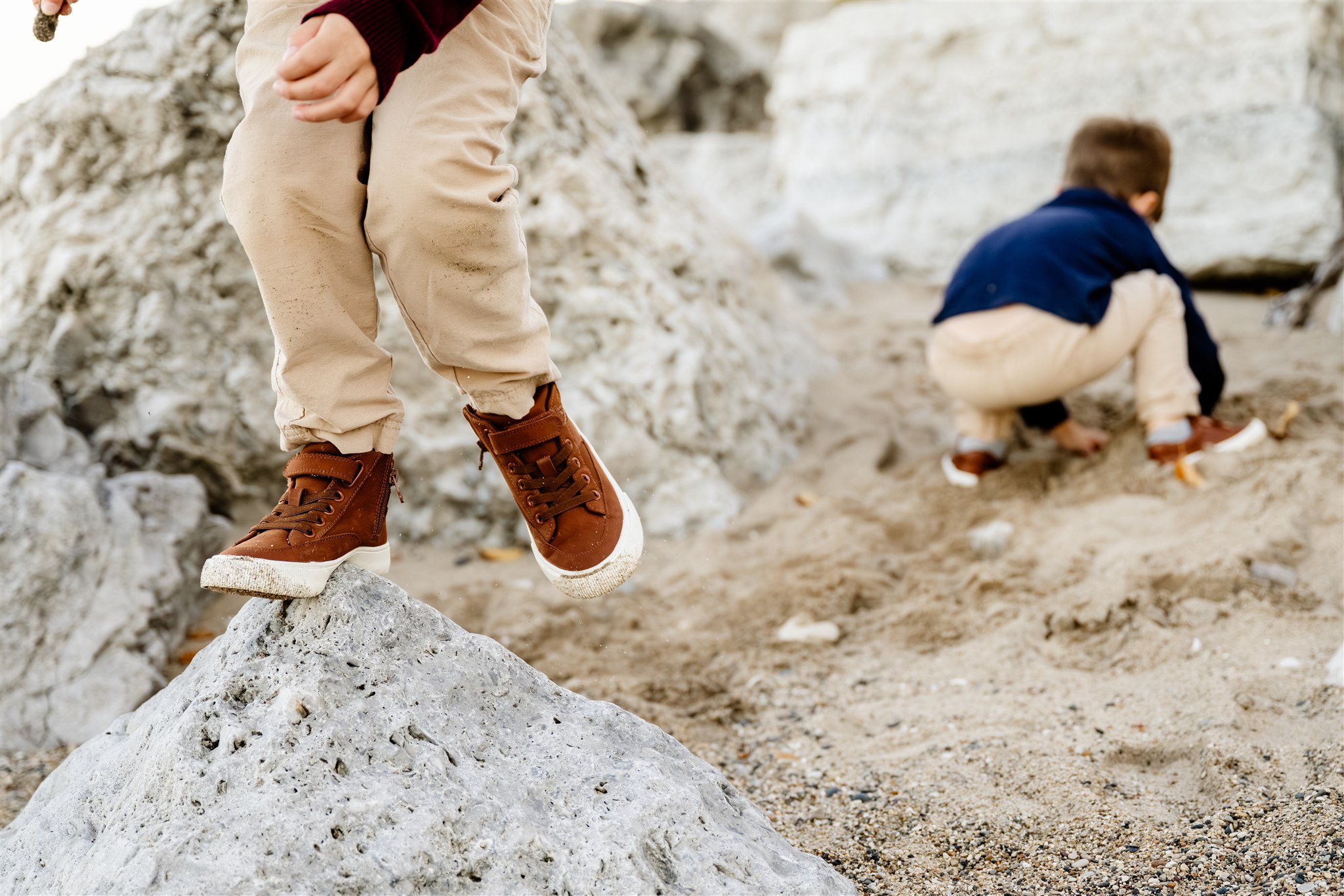Details of toddler brothers playing in sand between boulders after visiting playgrounds in North Shore