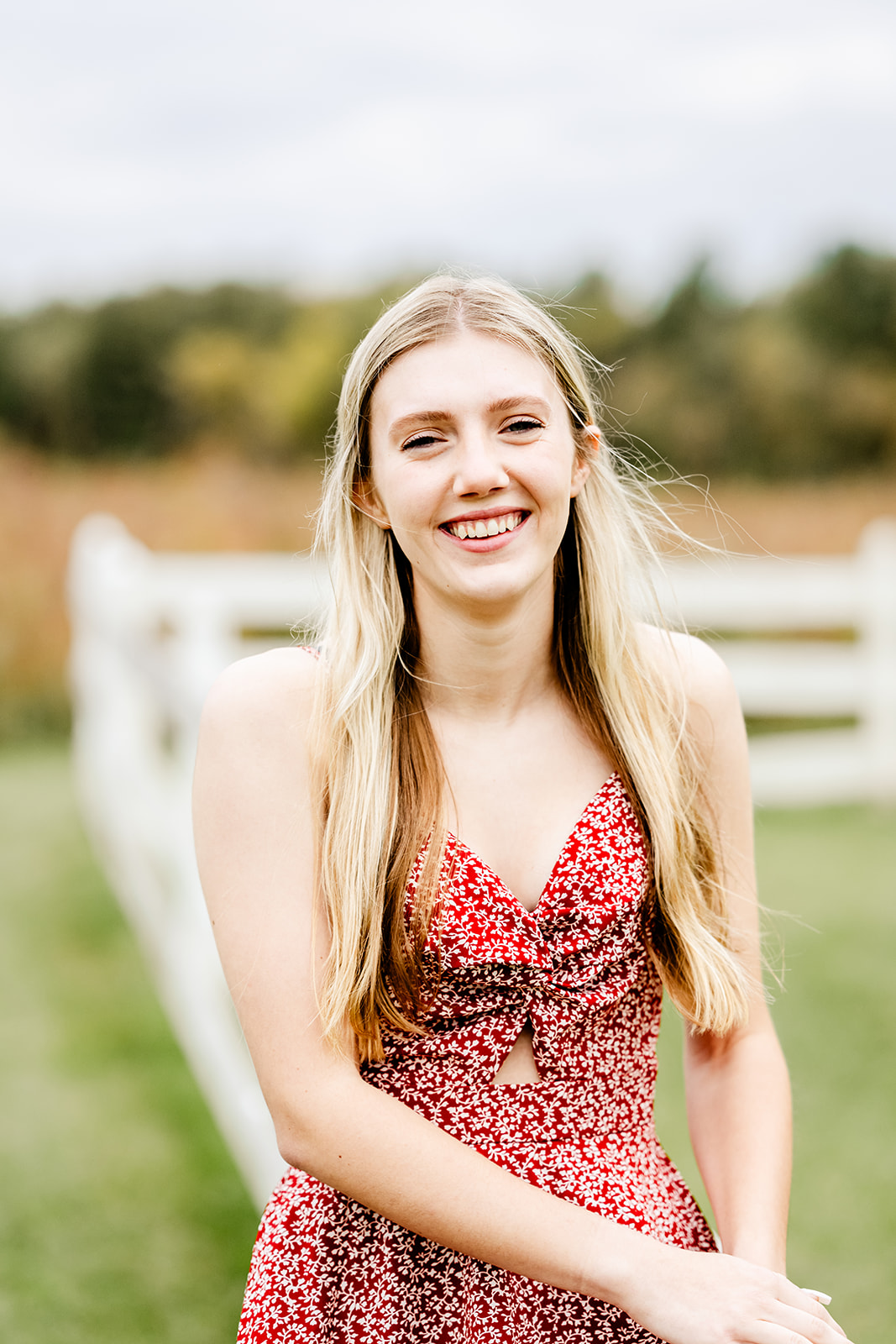 A happy high school grad in a red dress leans against a fence