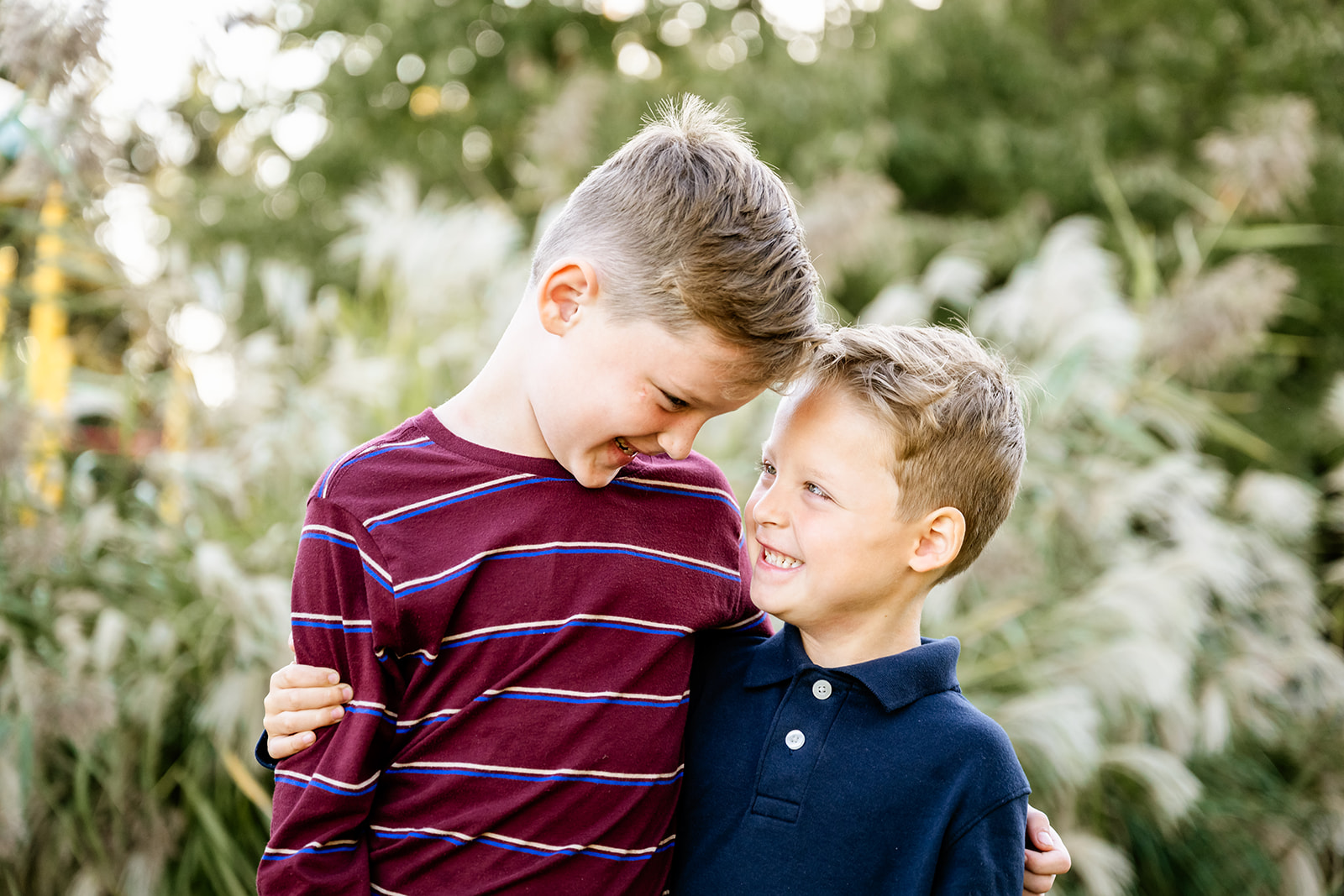 Toddler brothers smile at each other and hug in a garden at sunset in blue and red