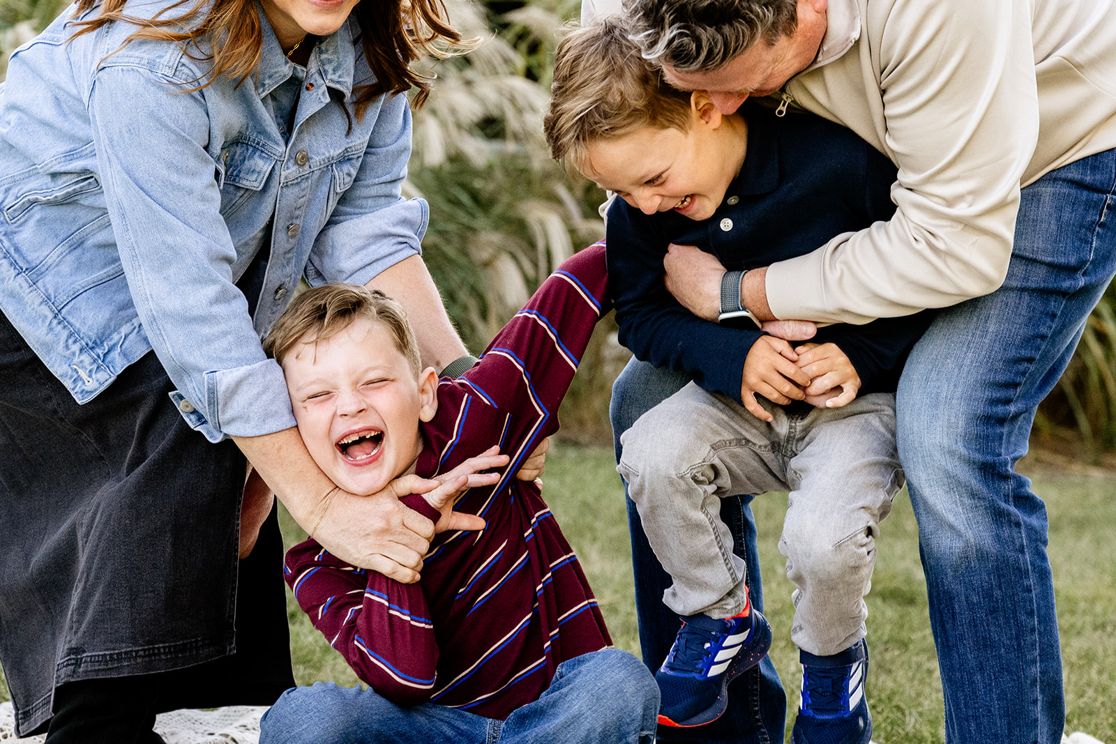 Toddler brothers are tickled by mom and dad in a park lawn at sunset after speech therapy in Chicago