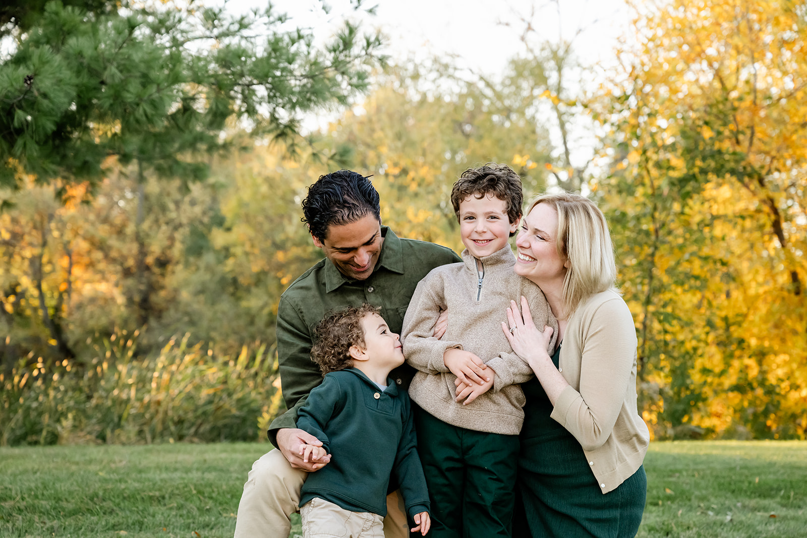 A mom and dad laugh with their toddler sons in a park lawn at sunset