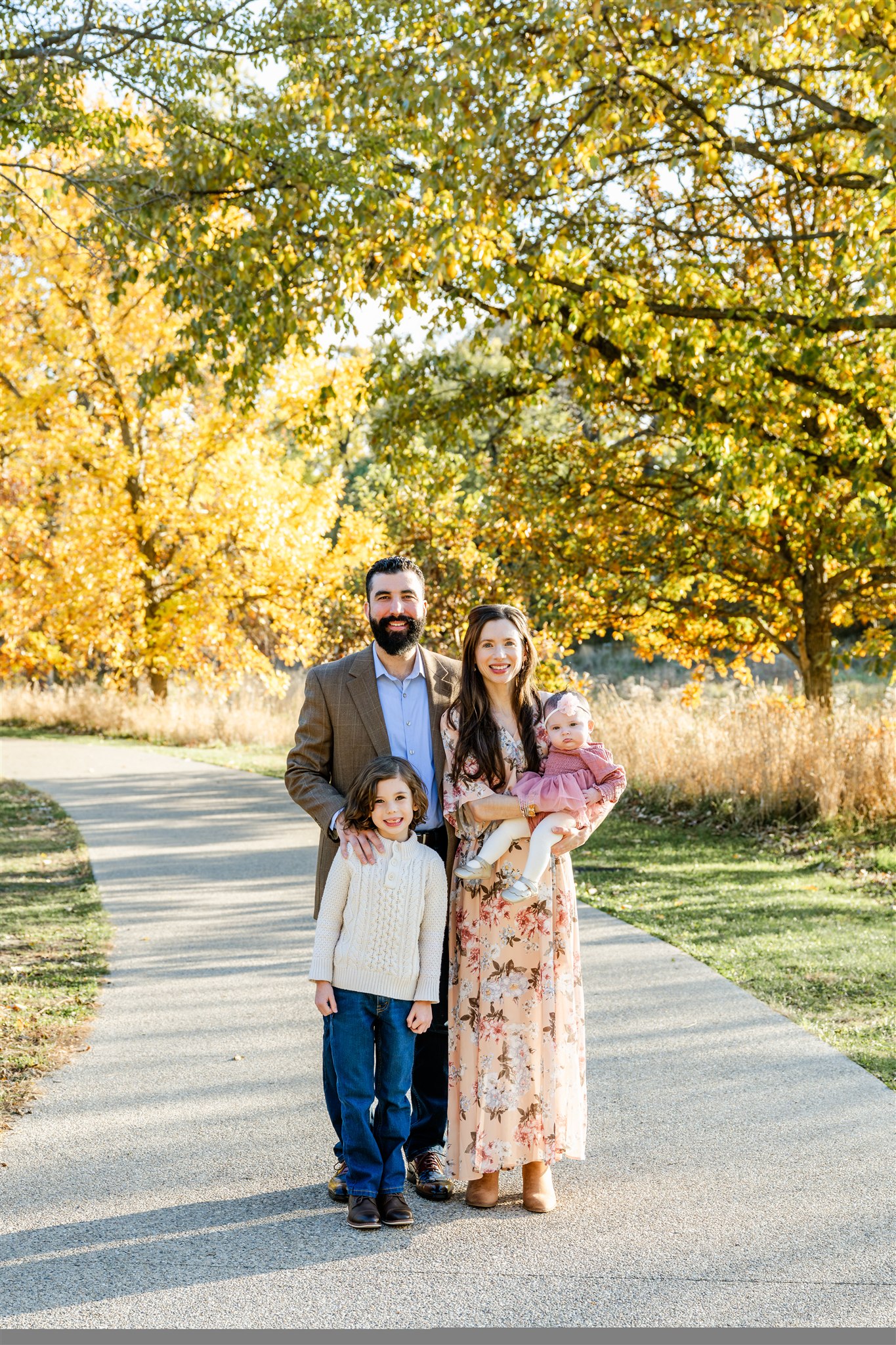 Happy mom and dad stand in a park sidewalk with their toddler son and daughter after exploring birthday party venues in North Shore Chicago
