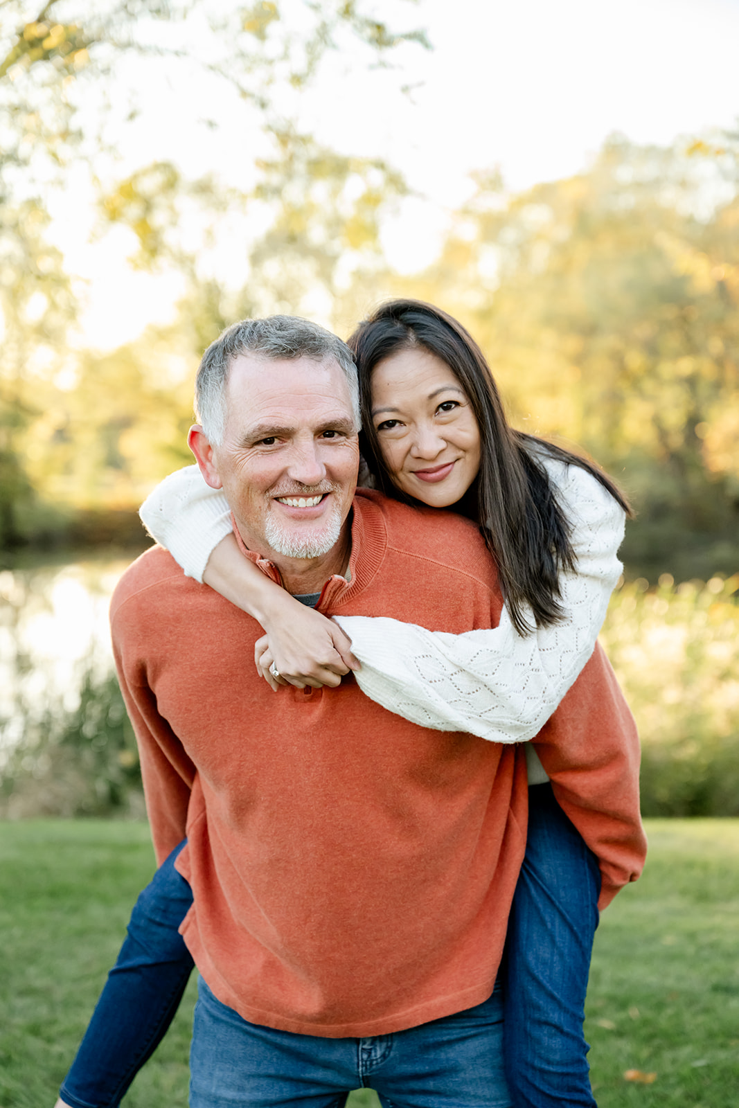 A woman in a white sweater is given a piggy back ride by her husband in a park after enjoying date night ideas in Naperville