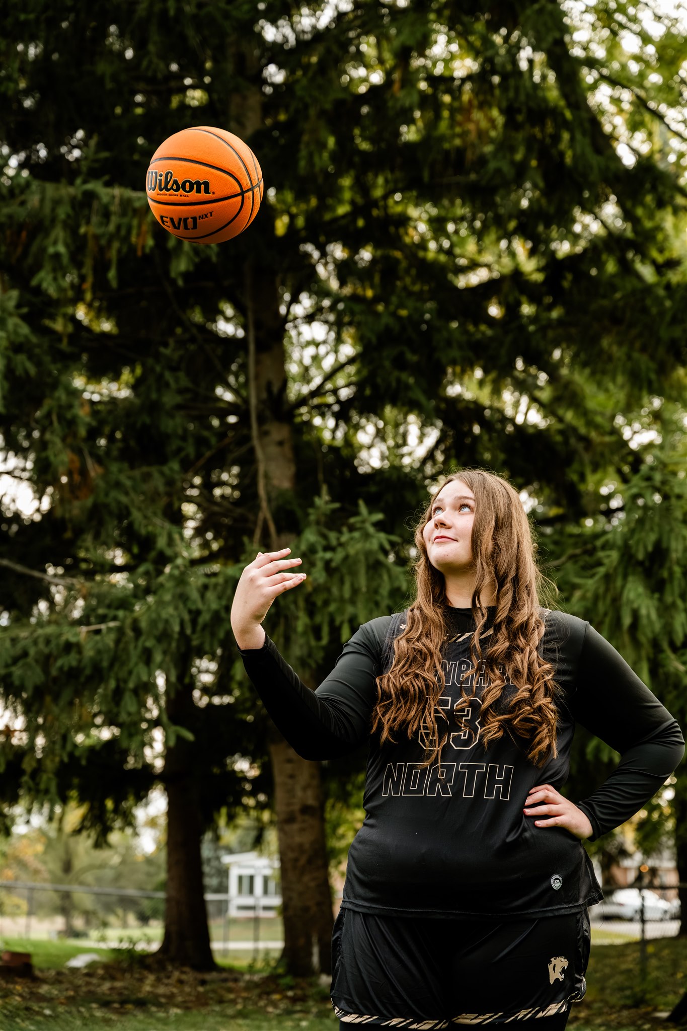 A high school senior tosses a basketball in the air with a hand on her hip in her black uniform