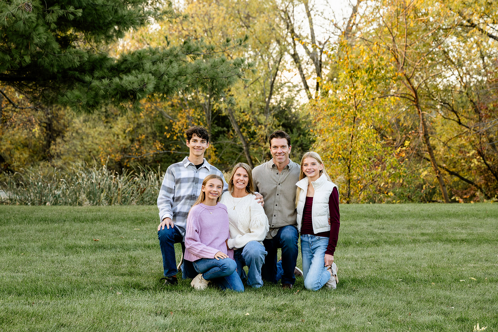 Mom and dad kneel next to their teenage son and two teenage daughters in a park after they visit kid friendly trails in naperville.
