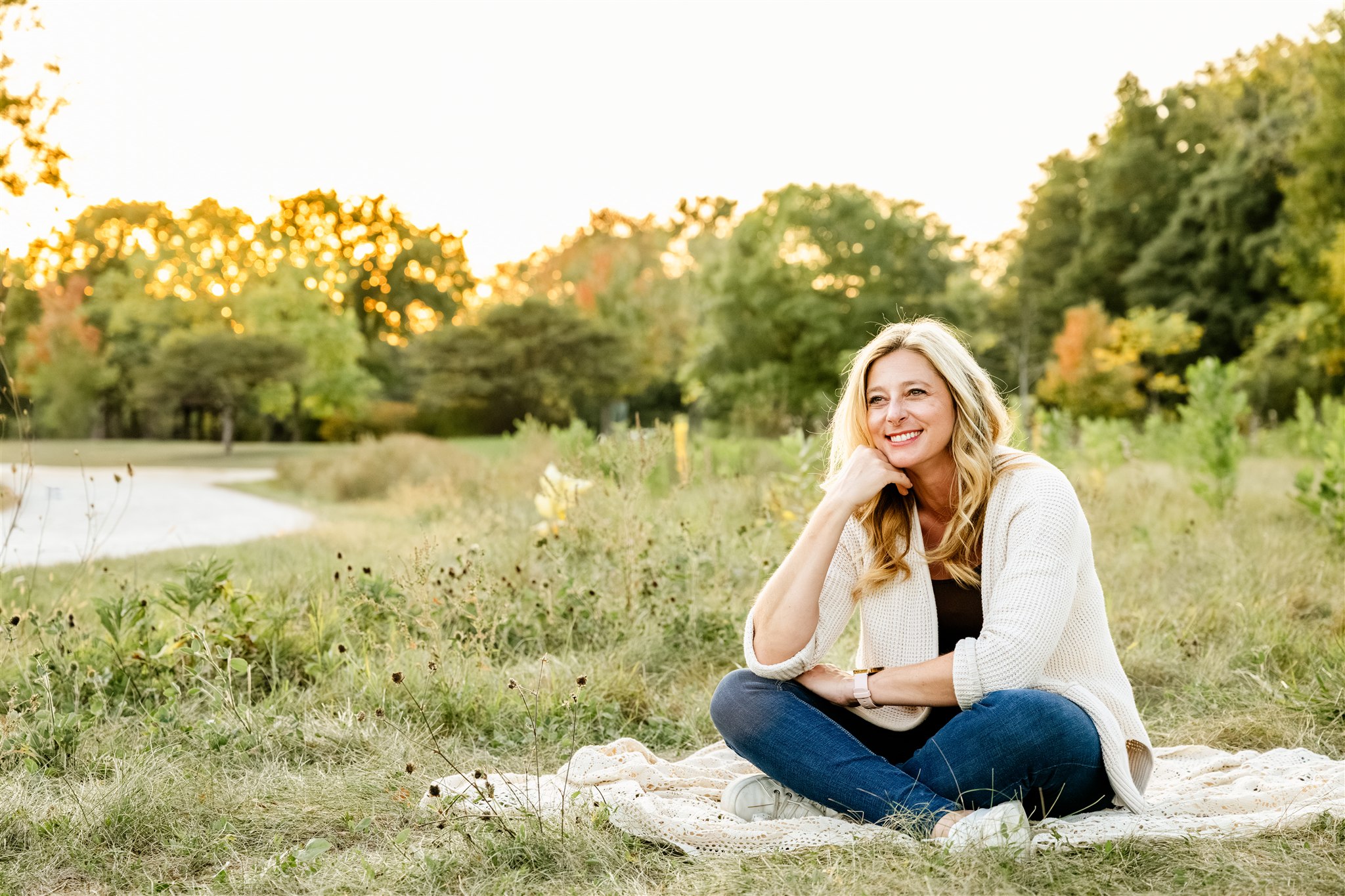 A lady sits on a beige blanket in a park as she smiles and stares into the distance after her pilates class in chicago.