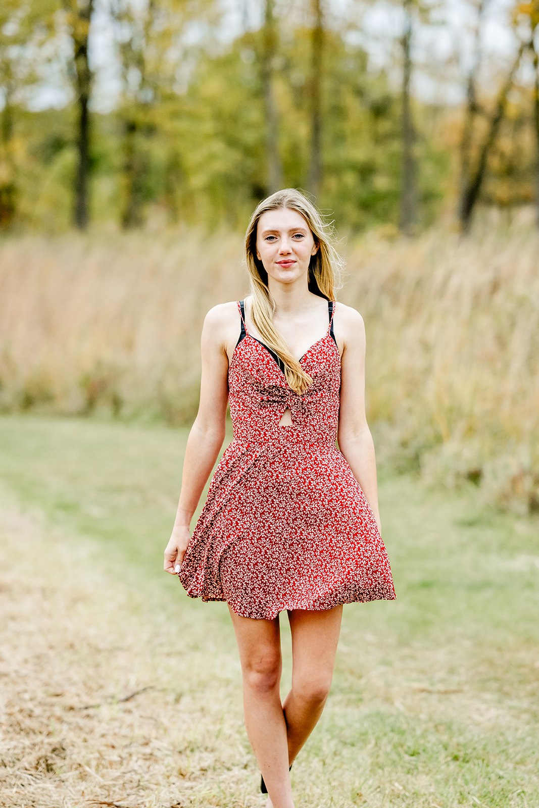 A smiling high school senior in a red summer dress walks in a park trail at sunset after trying on prom dresses in North Shore Chicago