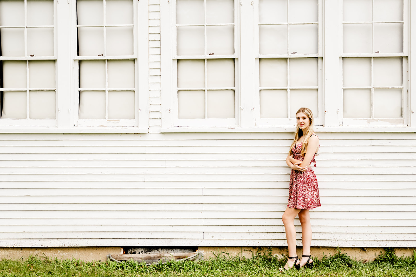 A high school senior in a like red dress stands against a rustic old building with arms crossed after shopping for prom dresses in North Shore Chicago