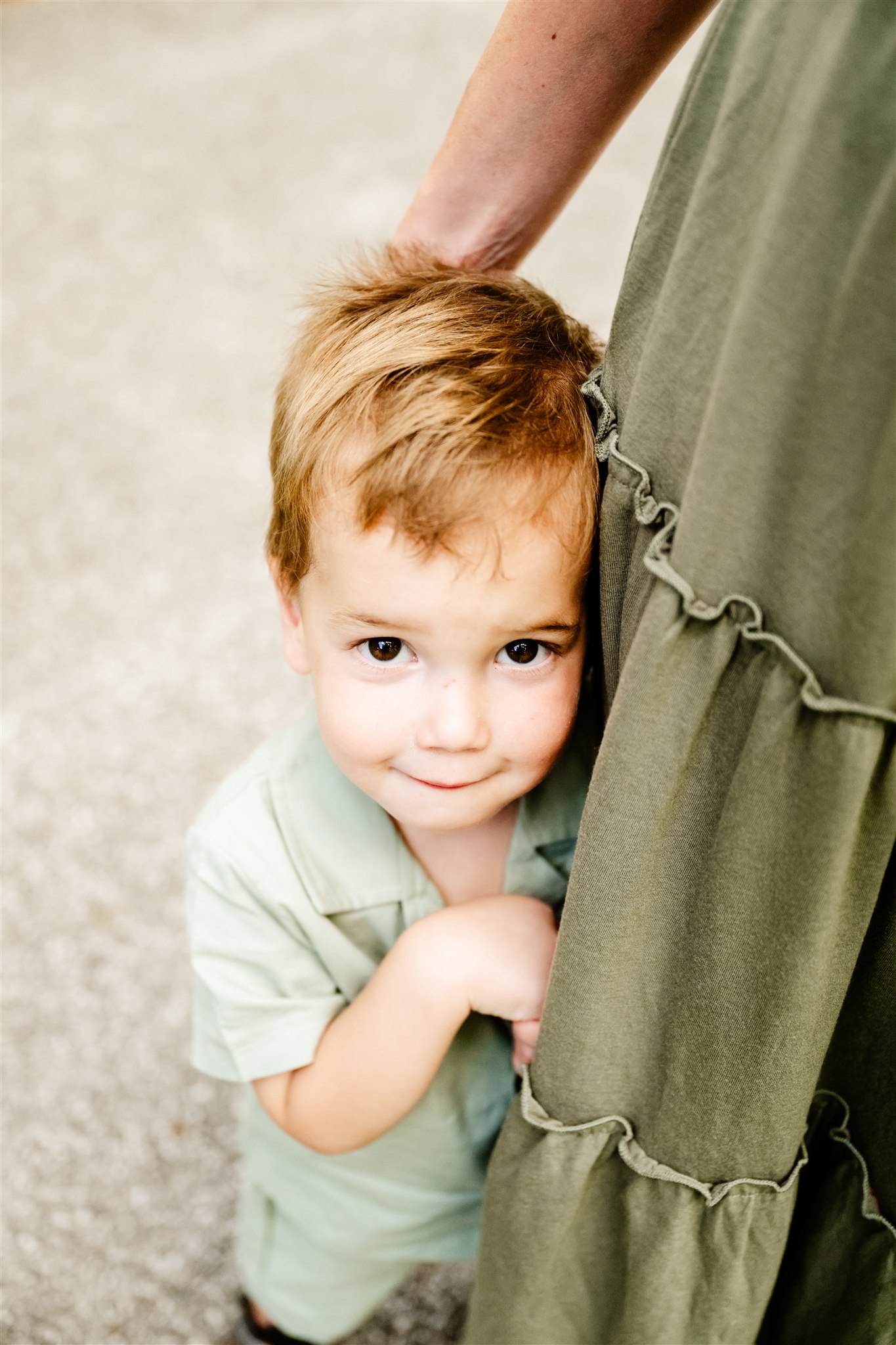 a young boy in a green shirt smiles as he clings onto his mom wearing a green dress.