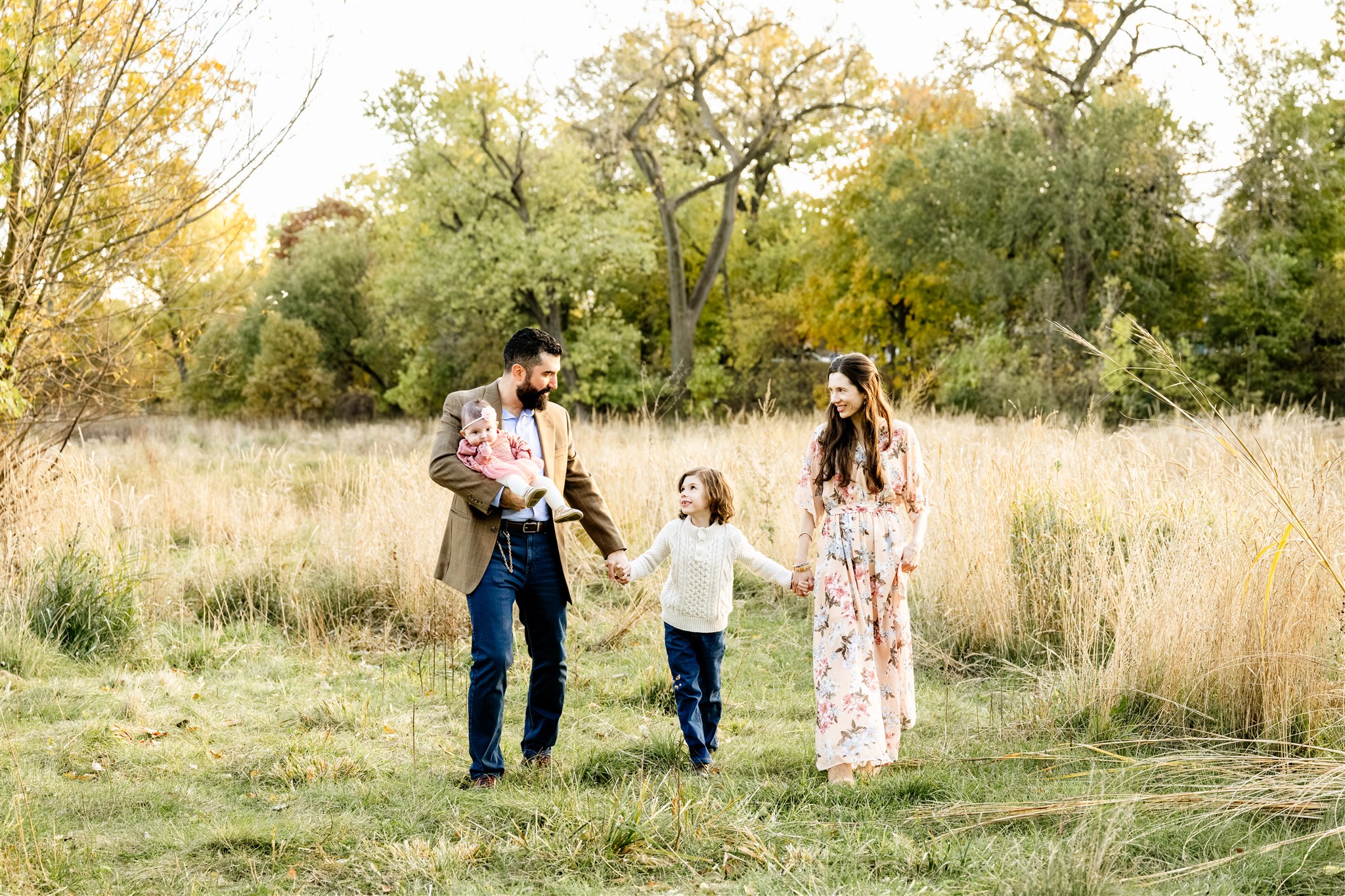 A young boy walks holding hands with mom and dad in a park trail through tall golden grass at sunset