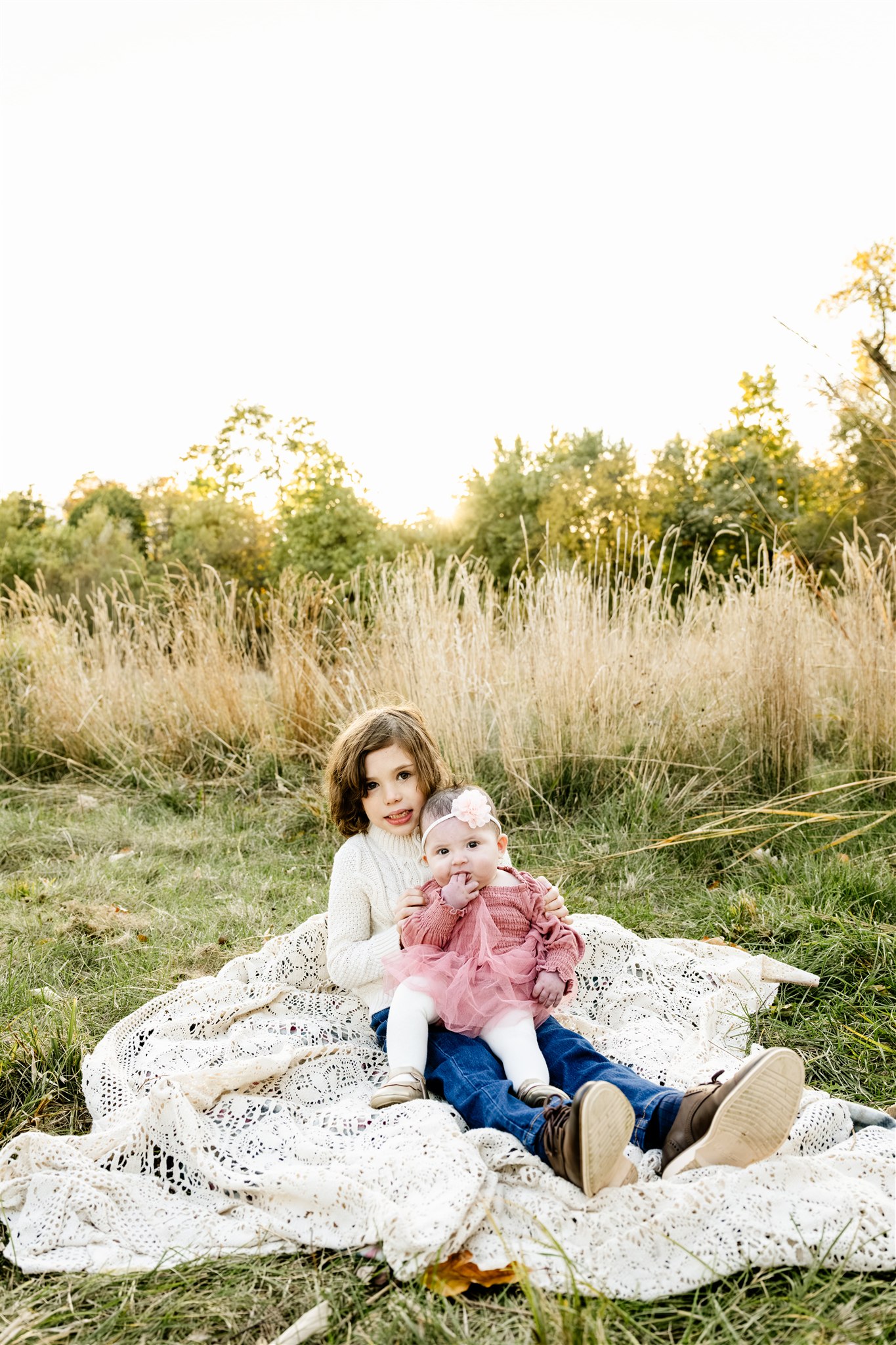 A young boy in a white sweater sitting in a park lawn with his baby sister in a pink dress after visiting childrens boutiques in North Shore Chicago