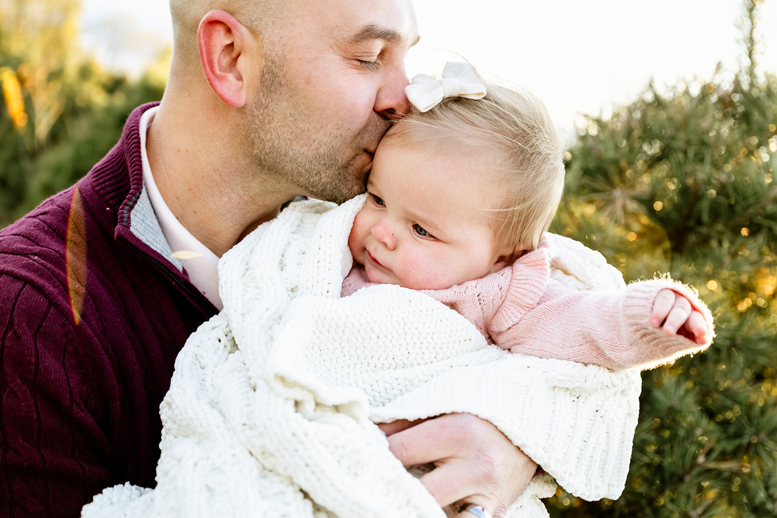 A happy dad kisses the head of his baby daughter in his arms at sunset after shopping for christening gowns in Naperville