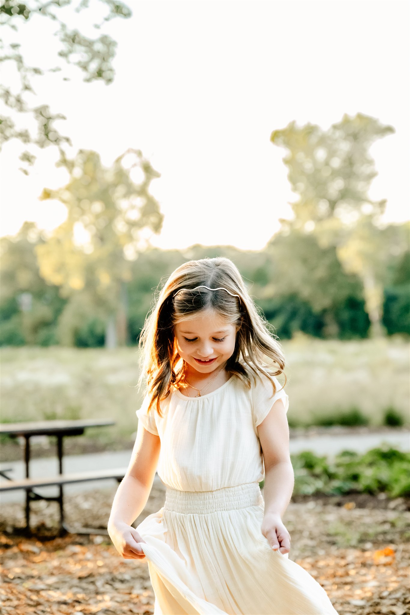 A happy toddler girl in a white dress plays in a park at sunset after some dance classes in Naperville