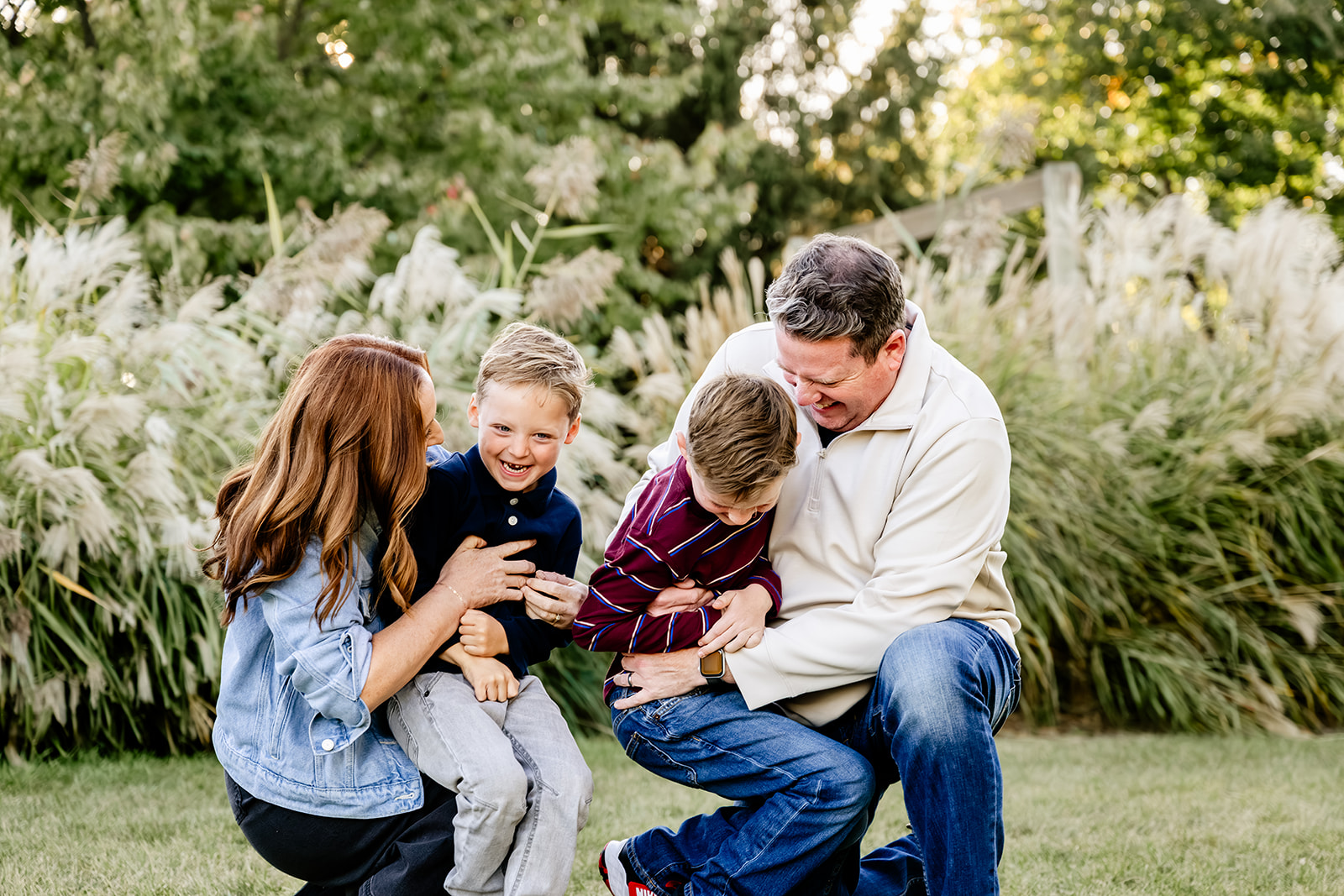 Giggling toddler brothers are tickled by mom and dad in a park lawn at sunset as everyone laughs after finding Montessori Schools in North Shore